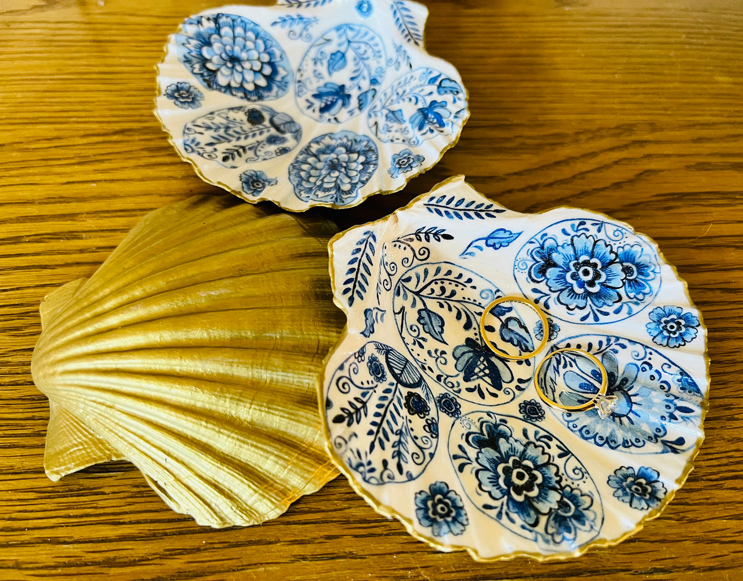 Handmade Dorset scallop shell trinket dishes featuring vintage inspired blue and white egg artwork with hand-painted gold leaf edging and glossy crystal clear resin. Elegant coastal jewellery dishes styled with Nordic and Scandinavian inspired porcelain patterns, photographed on soft neutral backgrounds with luxurious gilded detailing.