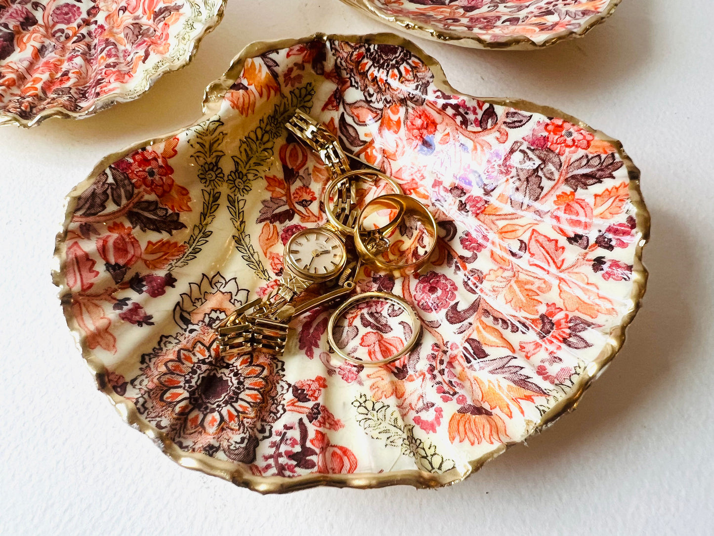 Handmade Dorset scallop shell trinket dish featuring a William Morris inspired pink floral botanical design in coral, berry and soft gold tones. Decorative jewellery holder finished with hand-applied liquid gold leaf edging and glossy resin. Heritage style coastal décor shell dish with romantic English country house aesthetic, styled as a ring holder and elegant vanity accessory.