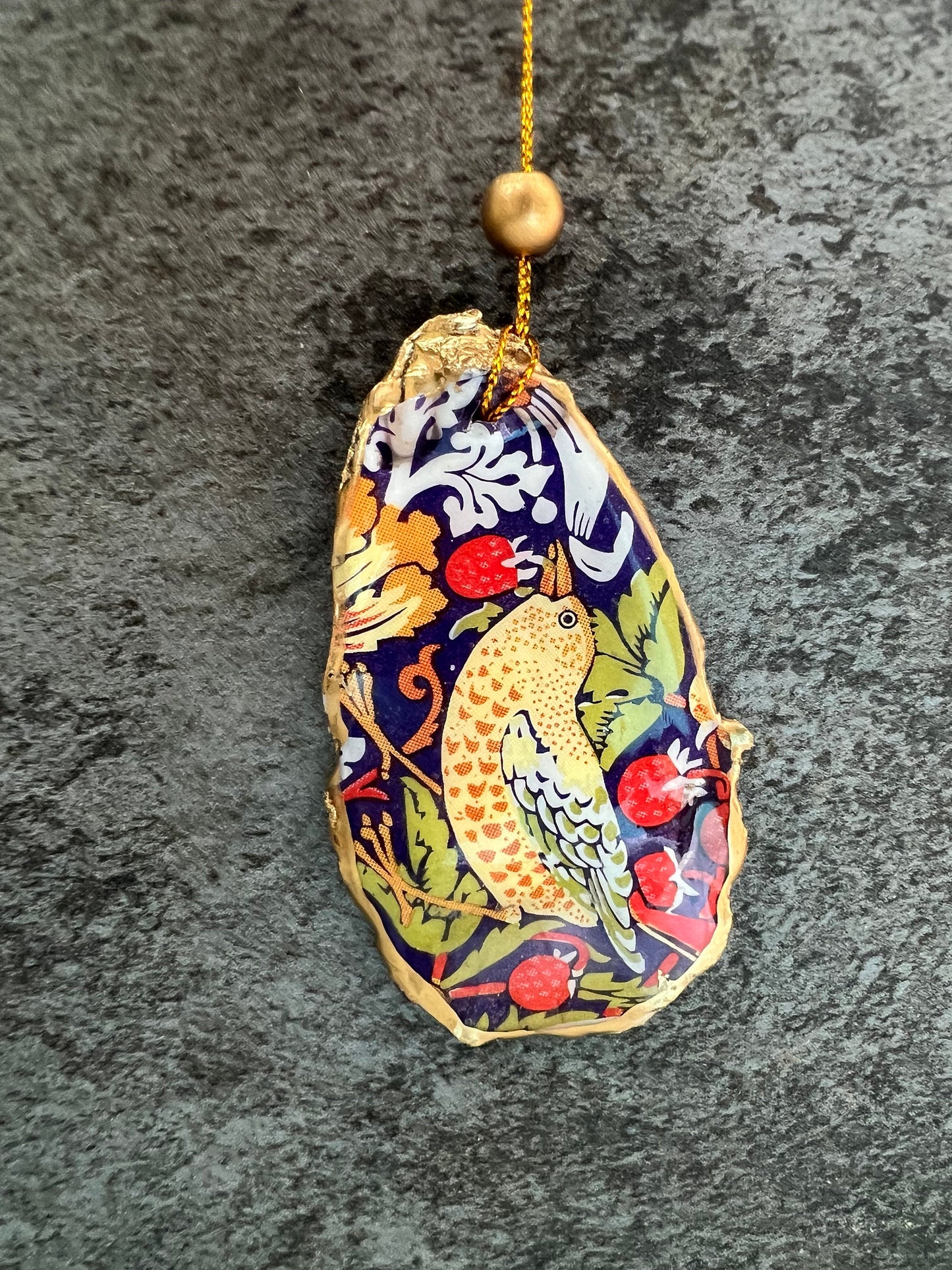 Handmade flat oyster shell ornaments decorated with William Morris Red Strawberry Thief design. Each Dorset shell has a natural pearl finish, gilded with liquid gold leaf on the rim and back, and sealed with glossy resin for durability and shine. Pre-drilled with gold string and bead for easy hanging. Available individually, as a set of 3, or set of 6. Unique coastal-inspired decorations, perfect as Christmas tree ornaments, wedding favours, bridesmaid gifts, or handmade William Morris presents.