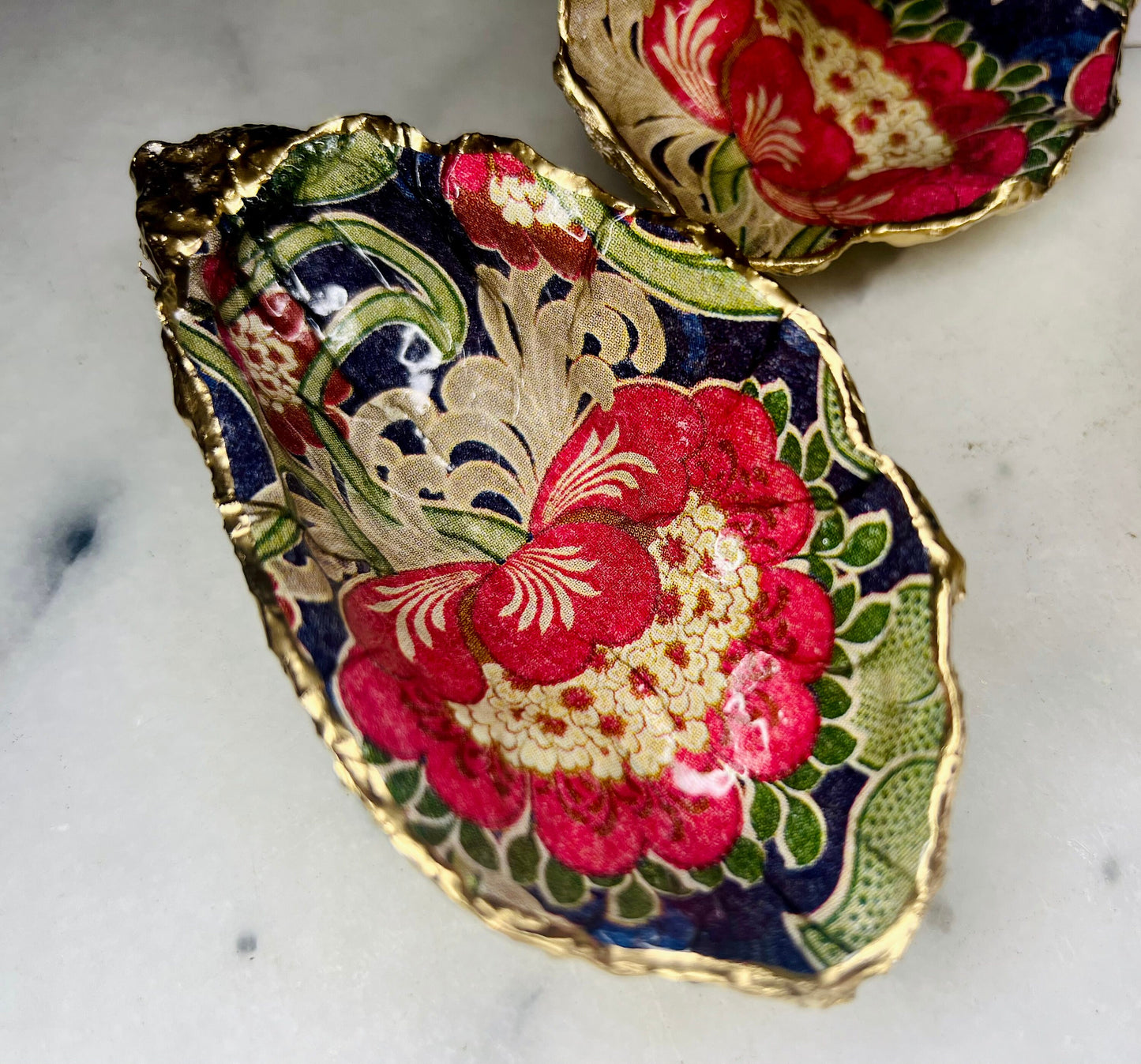 Handmade oyster shell trinket dish featuring a retro floral botanical pattern in pink, red, navy, and olive tones with gold leaf edging and glossy resin finish. Vintage V&A inspired oyster shell jewellery dish styled as coastal cottagecore home décor.