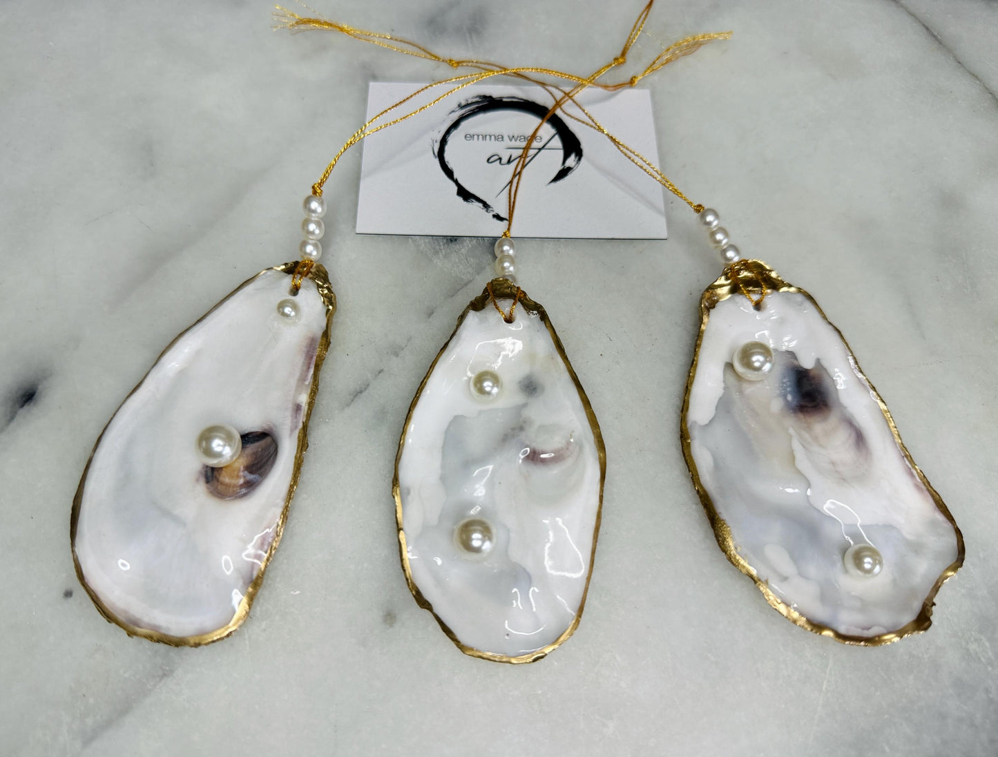 Luxury flat pearl oyster shell hanging ornaments handcrafted from natural Dorset oyster shells with glossy pearlescent interiors, two Swarovski pearls per ornament and hand-painted gold leaf edging. Elegant coastal hanging decor finished in crystal clear resin with gold hanging cord and pearl bead details. Available individually or as a set of three. Perfect for beach house interiors, luxury bathroom styling, wedding gifts, coastal Christmas decor and year-round shell home decor.