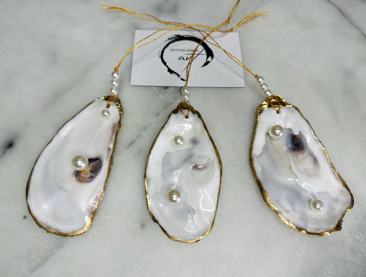 Luxury flat pearl oyster shell hanging ornaments handcrafted from natural Dorset oyster shells with glossy pearlescent interiors, two Swarovski pearls per ornament and hand-painted gold leaf edging. Elegant coastal hanging decor finished in crystal clear resin with gold hanging cord and pearl bead details. Available individually or as a set of three. Perfect for beach house interiors, luxury bathroom styling, wedding gifts, coastal Christmas decor and year-round shell home decor.