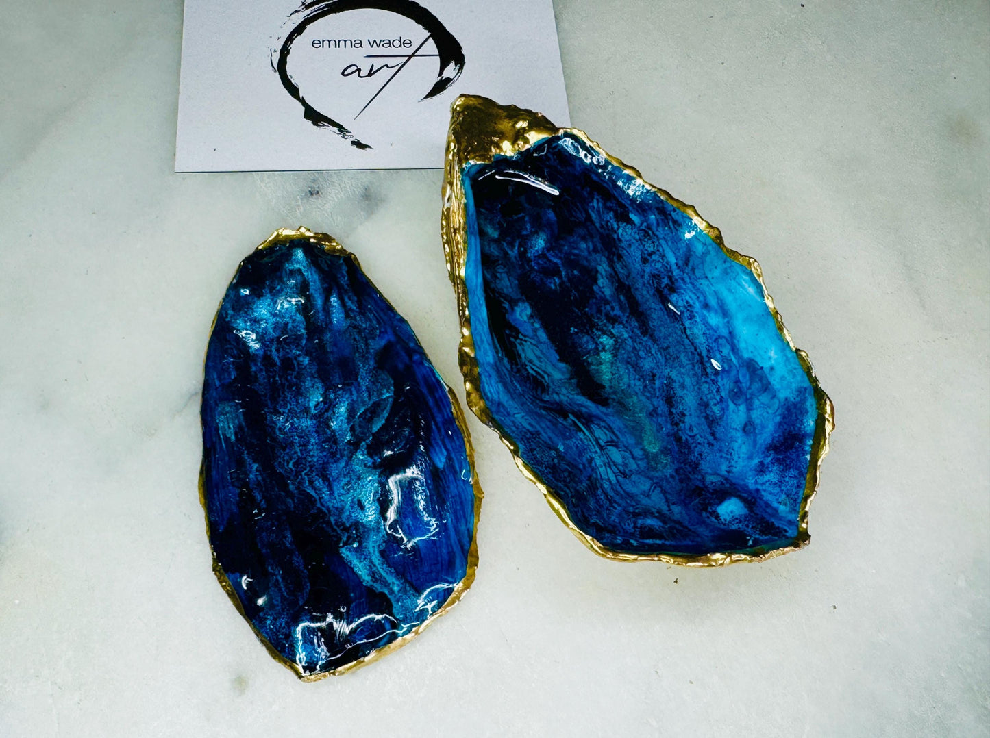 Blue oyster shell ring box, hand painted to resemble ocean waves in rich blue tones with metallic detail and finished with gold leaf edges. Includes a matching painted lid. Each shell is approx. 10cm and crafted from Dorset coastlines, making every piece unique. A stunning ocean-inspired jewellery box, ring bearer box, or proposal ring holder. Perfect for weddings, engagements, anniversaries, or as a keepsake gift for someone special who loves the sea.