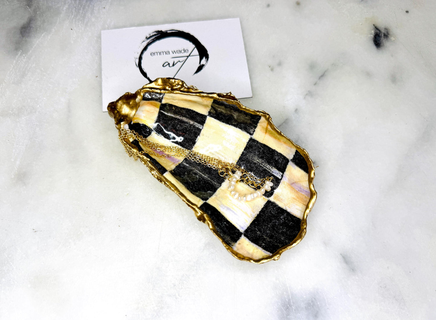 Black and gold chequered oyster shell dish with liquid gold leaf edging and glossy resin finish. A unique oyster ring dish, oyster ring tray, or shell jewellery organiser for rings, earrings, and cufflinks. This handmade trinket tray doubles as a jewellery dish or decorative coastal accent. Crafted from Dorset shells, each piece is one of a kind. A thoughtful handmade gift for weddings, anniversaries, birthdays, Christmas, bridesmaids, or new home celebrations.