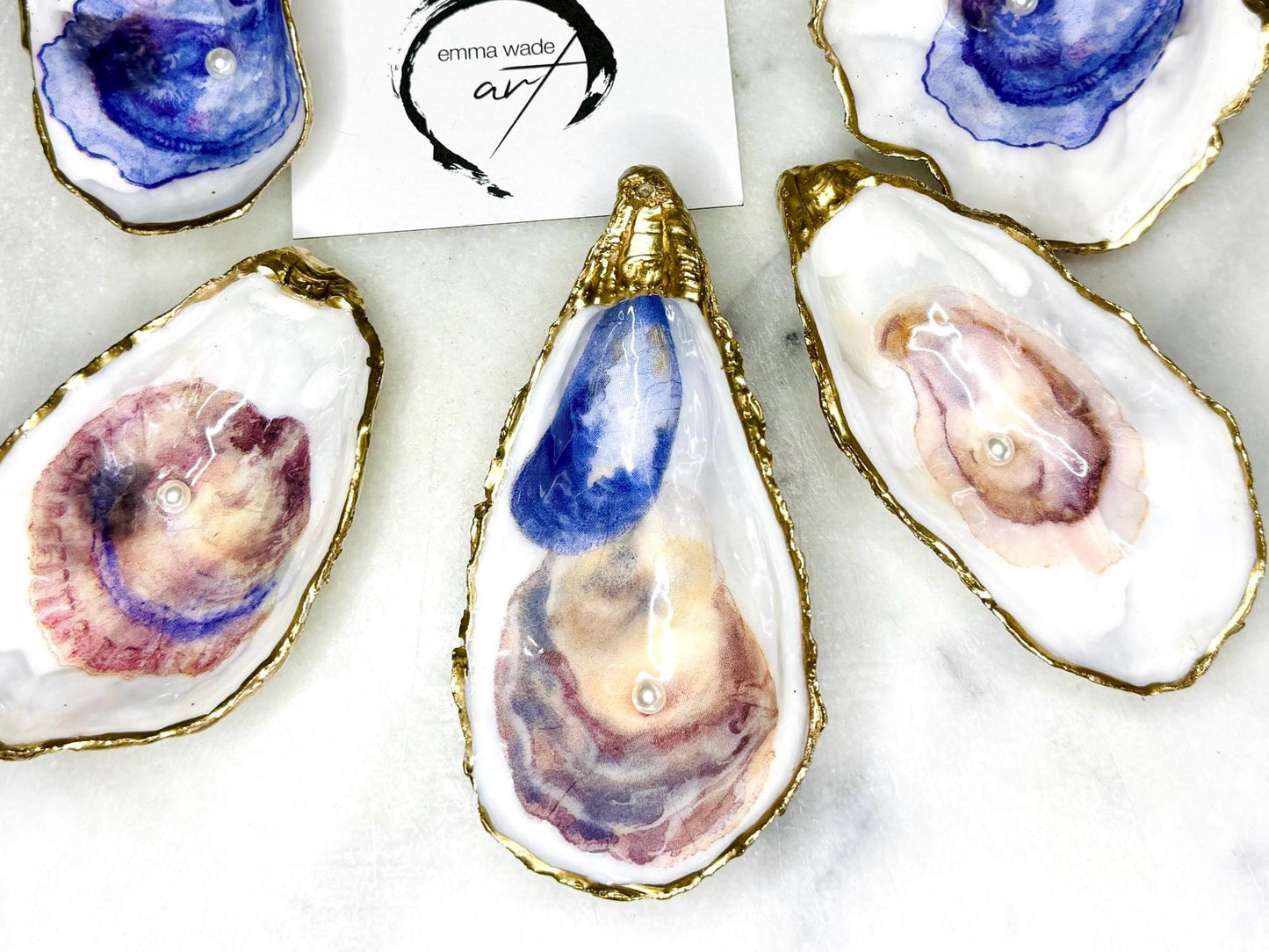 Handmade Dorset oyster shell trinket dish featuring a blue and beige watercolour oyster illustration with Swarovski pearl detail, finished with hand-applied gold leaf edging and glossy resin. Coastal-inspired jewellery dish and ring holder available in multiple sizes including XL oyster shells. Elegant handmade coastal décor gift ideal for weddings, birthdays, anniversaries, and luxury beach house interiors.