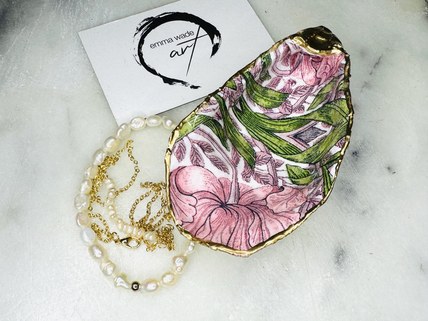 Single handcrafted Dorset oyster shell trinket dish featuring the William Morris Pink Pimpernel design in pink and green tones, edged with liquid gold leaf and sealed in glossy resin. Sold individually, this natural oyster shell jewellery holder is ideal for rings or earrings and makes a unique coastal gift or wedding favour.