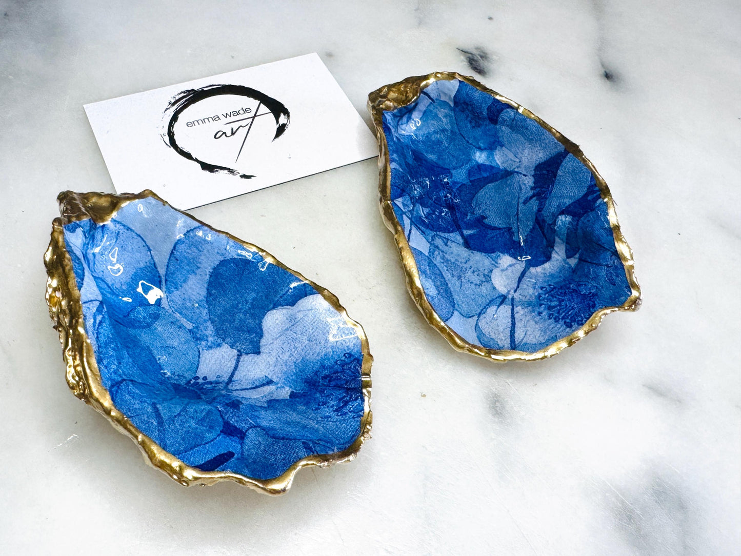 Pair of oyster shell salt and pepper dishes with deep blue watercolour flower design, finished with gold leaf trim and glossy seal. Handmade from Dorset oyster shells, each dish is unique with natural variations. A beautiful oyster shell salt gift set, also available with matching gold crystal spoons for a finishing touch. Perfect for weddings, anniversaries, dinner parties, or as a handmade gift for birthdays, Christmas, or housewarmings. Elegant coastal tableware and decor piece.