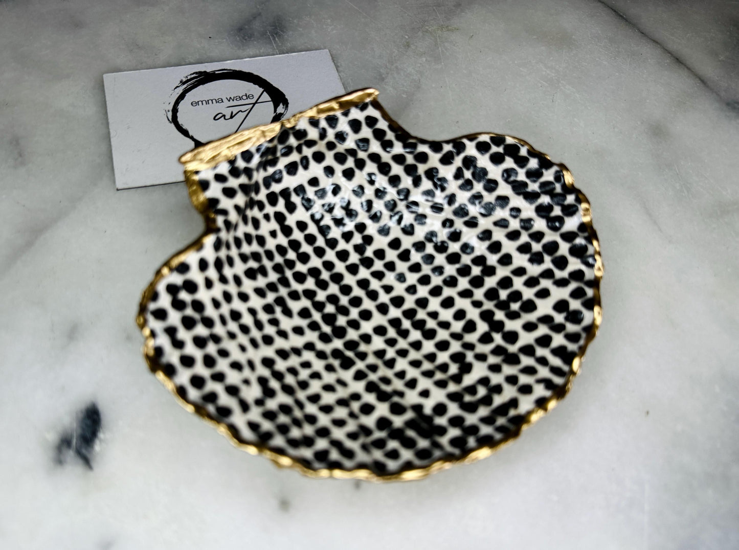 Handcrafted black and white dotted Dorset scallop shell trinket dish, gilded with real gold leaf and sealed in crystal-clear resin. Perfect as a jewellery holder, cufflink tray, tea light holder, or coastal home accent. Each eco-friendly shell is ethically sourced from the Dorset coastline, individually hand finished in Surrey, and presented in a sustainable gift box. A thoughtful handmade gift for ocean lovers, weddings, birthdays, or coastal home décor.