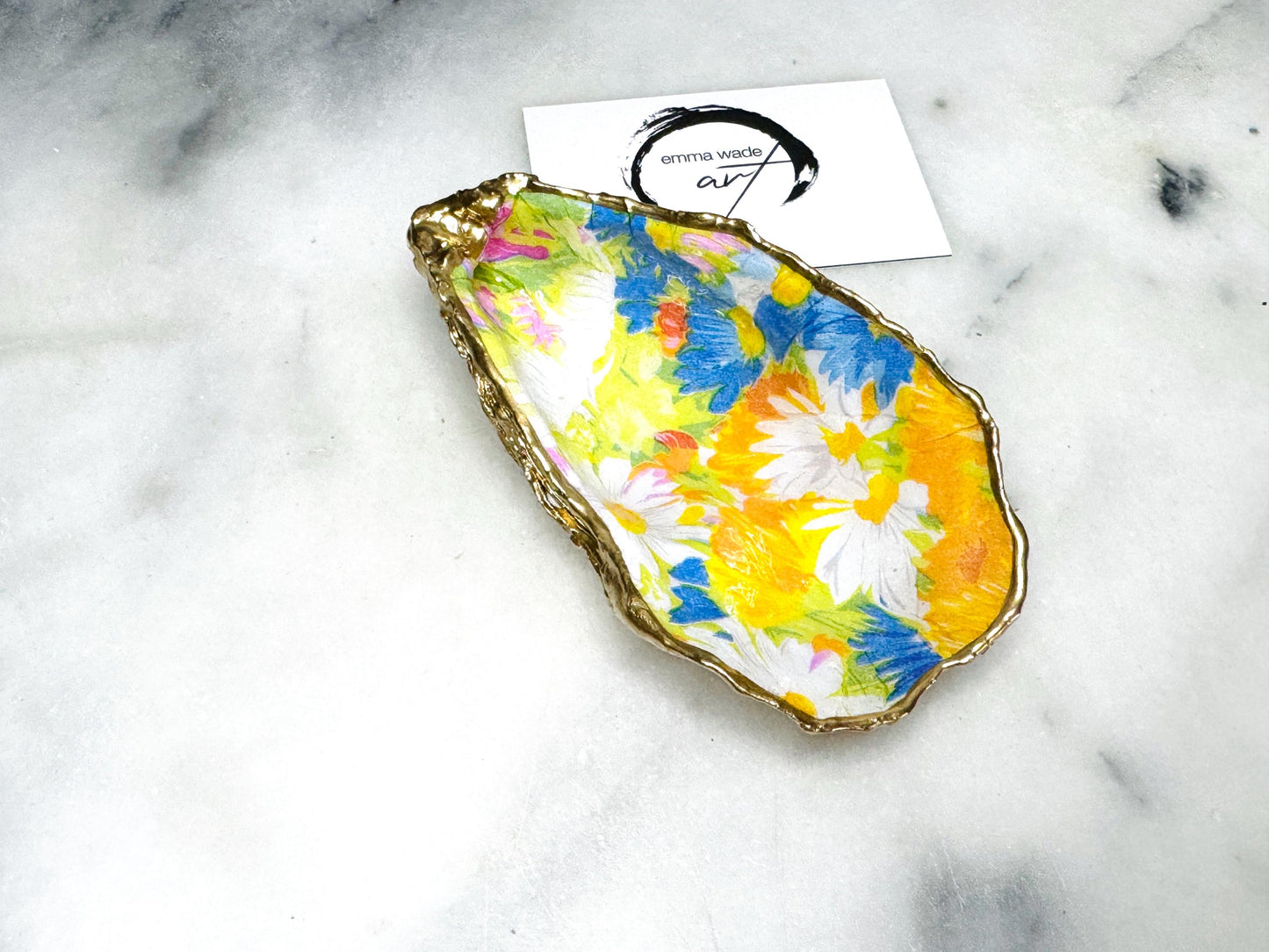 Handmade Dorset oyster shell trinket dish featuring colourful floral artwork in pink, yellow, orange, and blue tones with genuine gold leaf edging and glossy resin finish. Coastal jewellery holder and vibrant floral home décor gift.