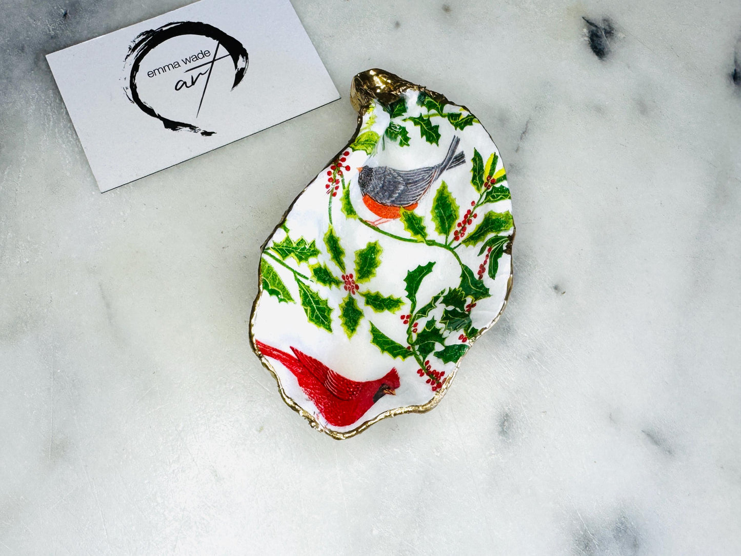 Handmade Dorset oyster shell Christmas ornament featuring red and orange winter birds perched amongst festive green foliage and berries. Coastal oyster shell trinket dish with hand applied gold leaf edging and glossy resin finish, styled as luxury Christmas décor. Sustainable handcrafted robin-inspired shell decoration available as hanging ornament or jewellery dish, inspired by British winter wildlife and the Dorset coastline.