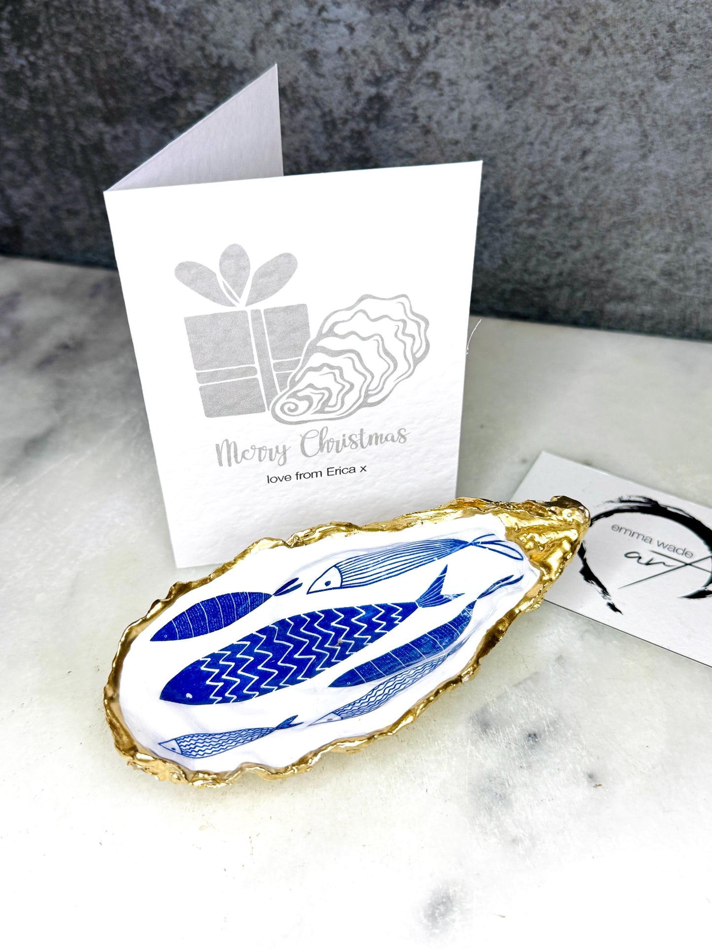 Luxury hand gilded Dorset oyster shell trinket dish featuring a refined blue fish motif, edged in liquid gold leaf and sealed in crystal clear resin. Sustainable coastal ring holder handmade by the artist in Surrey and presented in eco friendly branded gift packaging. Elegant beach house decor piece ideal for jewellery storage, wedding styling or sophisticated coastal interiors.