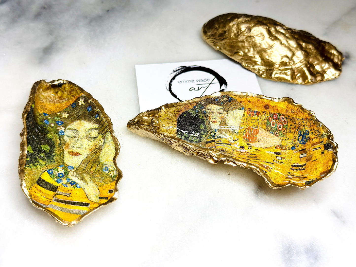 Pair of handmade Dorset oyster shell salt and pepper pinch pots inspired by Gustav Klimt’s The Kiss, decorated with rich gold artwork, hand-finished with liquid gold leaf, and sealed in crystal-hard glossy resin. Luxury coastal serving dishes with optional gold crystal spoons, perfect for weddings, anniversaries, dinner parties, and elegant table décor.