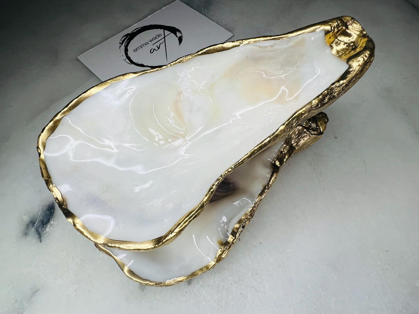 Extra large Dorset oyster shell serving dish set with natural pearl interior and hand-applied gold leaf edging, featuring a cupped XL oyster shell with matching flat shell base. Luxury coastal home décor ideal as a sugar dish, serving bowl, coffee station accessory, or elegant host gift. Handmade using sustainably sourced UK oyster shells and finished with glossy resin and optional gold serving accessories.