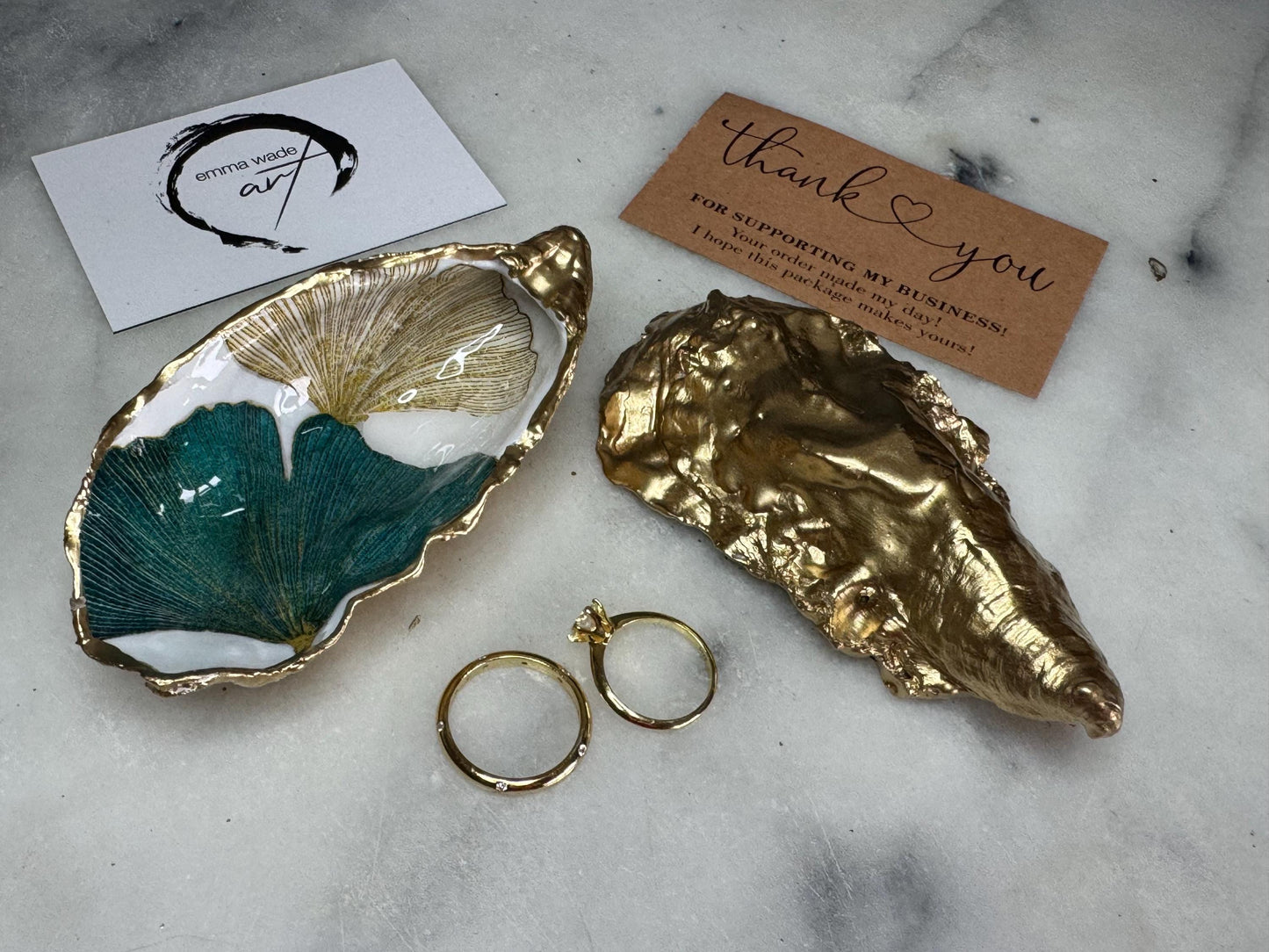 Handmade Dorset oyster shell ring dish featuring Japanese Ginkgo floral leaf artwork in emerald green, gold, and pearl tones with hand-applied liquid gold leaf edging. Luxury coastal jewellery tray sealed in glossy crystal-clear epoxy resin, styled with gold rings.