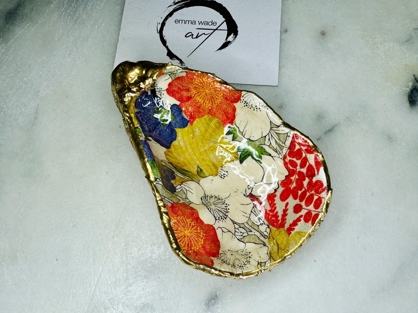 Handmade oyster shell trinket dish featuring a colourful Japanese kimono-style floral design applied with decoupage, finished with hand-gilded gold leaf edges and sealed in glossy clear resin. Natural Dorset oyster shell used as a jewellery dish or ring holder, photographed on a light surface, showcasing the vibrant flowers and luxury gold detailing. Ideal as coastal home decor or a unique handmade gift.
