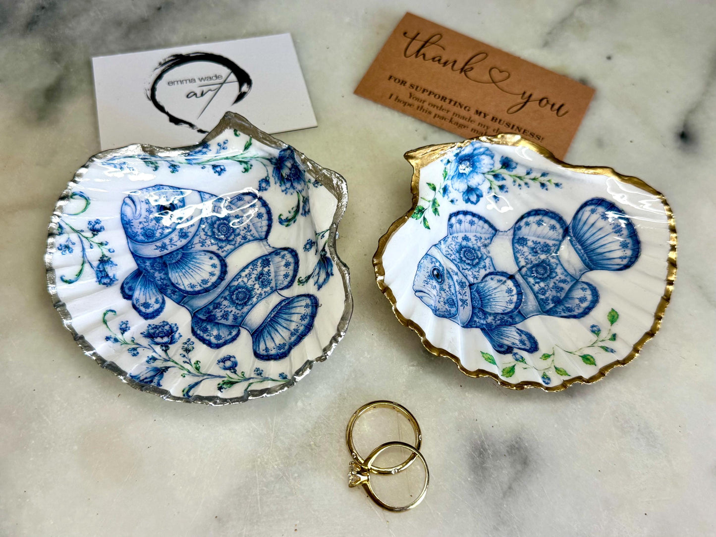Clownfish scallop shell trinket dish featuring an original illustrated Delft Blue design by Emma Wade ART. Natural scallop shell finished with gold leaf or silver leaf edging and a crystal-clear glossy resin coating. Coastal jewellery tray, Floral ring holder and ocean-inspired gift for fish and sea lovers, beach house décor, weddings, bridesmaids and nautical homes.