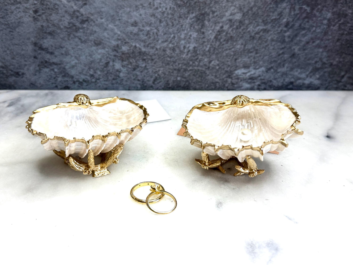 Luxury natural Spiny Cockle shell proposal and wedding ring dish on an ornate gold metal stand, available with or without an inset Swarovski pearl ring holder. Pearlescent shell approximately 8–9cm wide with a hand-gilded liquid gold leaf rim, delicate gold embellishments and crystal-clear resin finish. Handmade luxury jewellery holder, engagement ring dish, bridal keepsake and coastal decor by Emma Wade ART.