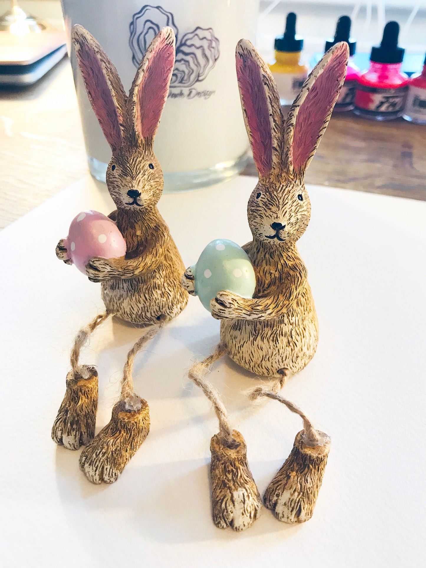 Hand-finished shelf sitting bunny ornament with dangling jute legs and polka dot egg. Available in pink or green. Perfect Easter rabbit shelf decoration, birthday gift, or home décor accessory. Cute animal figurine for rabbit lovers, Easter decorations, new home presents, or seasonal mantel styling.
