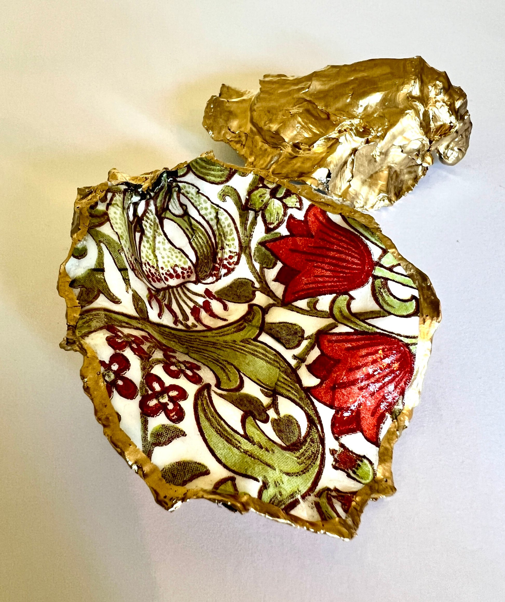 Handmade Dorset oyster shell ring dish featuring William Morris Golden Lily floral artwork in green, red and gold tones. Natural oyster shell trinket dish with pearlescent interior, hand-finished liquid gold leaf edging and glossy resin coating. Decorative jewellery holder and coastal heritage gift inspired by classic William Morris interiors and Arts and Crafts design.
