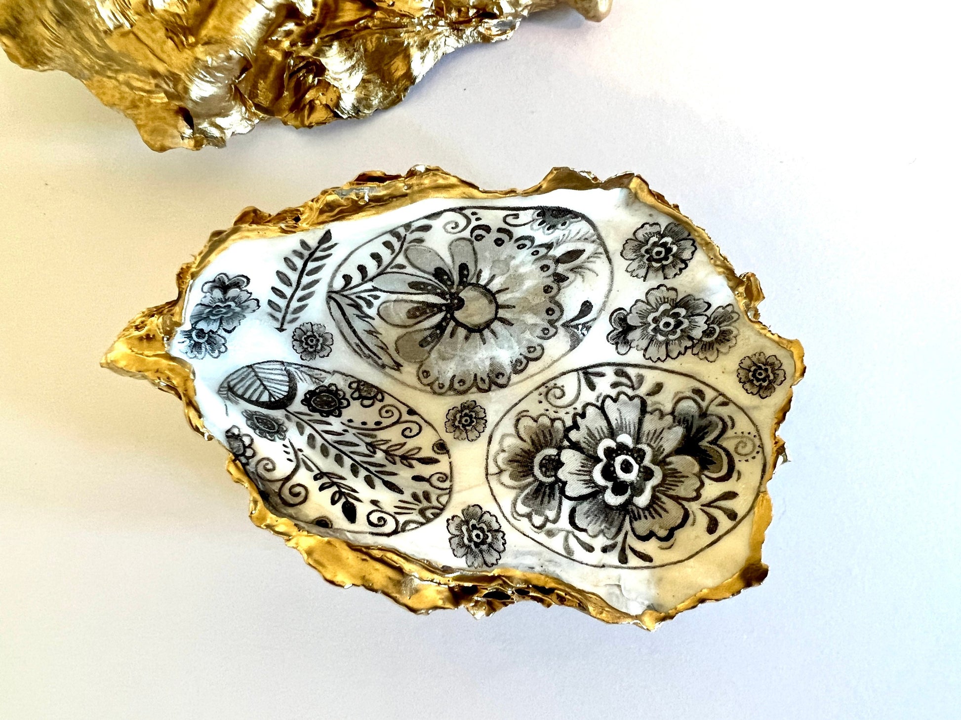 Handmade Dorset oyster shell dish featuring a decorative grey eggs design. Each oyster shell is finished with liquid gold leaf edging and reverse, sealed with crystal-clear resin for a glossy, durable shine. Unique and symbolic, the egg represents new life, fertility, hope, and luck, making this piece a thoughtful and meaningful gift. Ideal as a jewellery dish, oyster ring holder, trinket tray, or keepsake ornament. A coastal-inspired handmade gift for anniversaries, Easter, or Christmas.