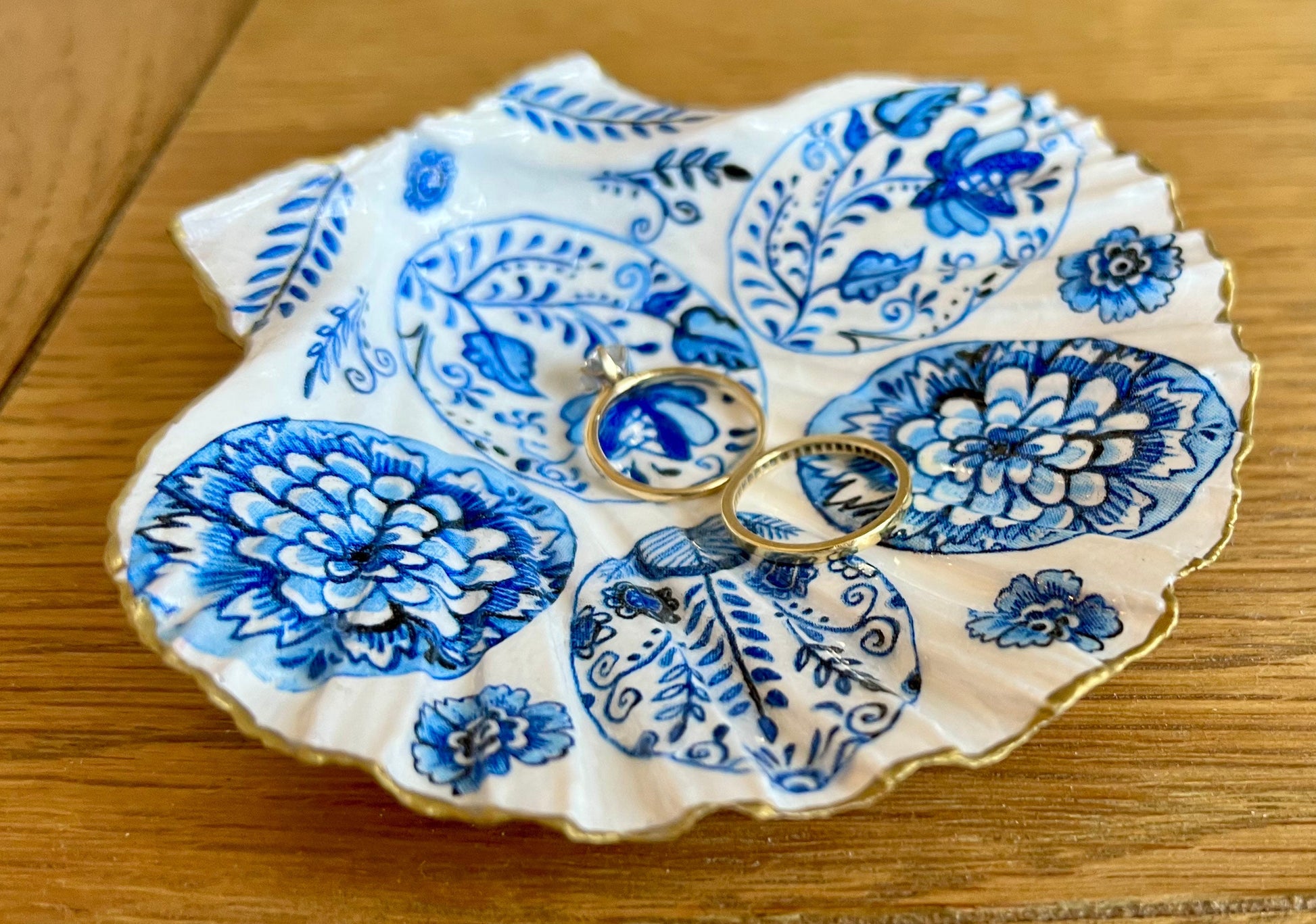 Handmade Dorset scallop shell trinket dishes featuring vintage inspired blue and white egg artwork with hand-painted gold leaf edging and glossy crystal clear resin. Elegant coastal jewellery dishes styled with Nordic and Scandinavian inspired porcelain patterns, photographed on soft neutral backgrounds with luxurious gilded detailing.