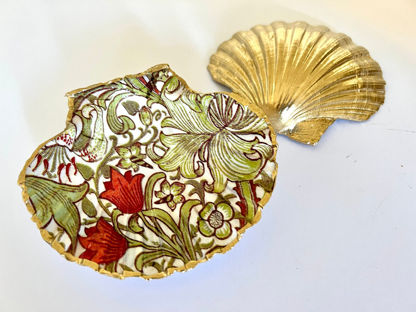 Handcrafted William Morris Golden Lily scallop shell ring holder featuring an elegant botanical floral pattern in green, cream and muted red tones. Decorative Dorset shell trinket dish finished with hand-painted gold leaf edging and sealed in glossy crystal resin for a luxurious shine. Coastal inspired jewellery tray and bedside catchall perfect for rings, earrings and keepsakes. Botanical shell decor for elegant interiors, cottage style homes, thoughtful handmade gifting.