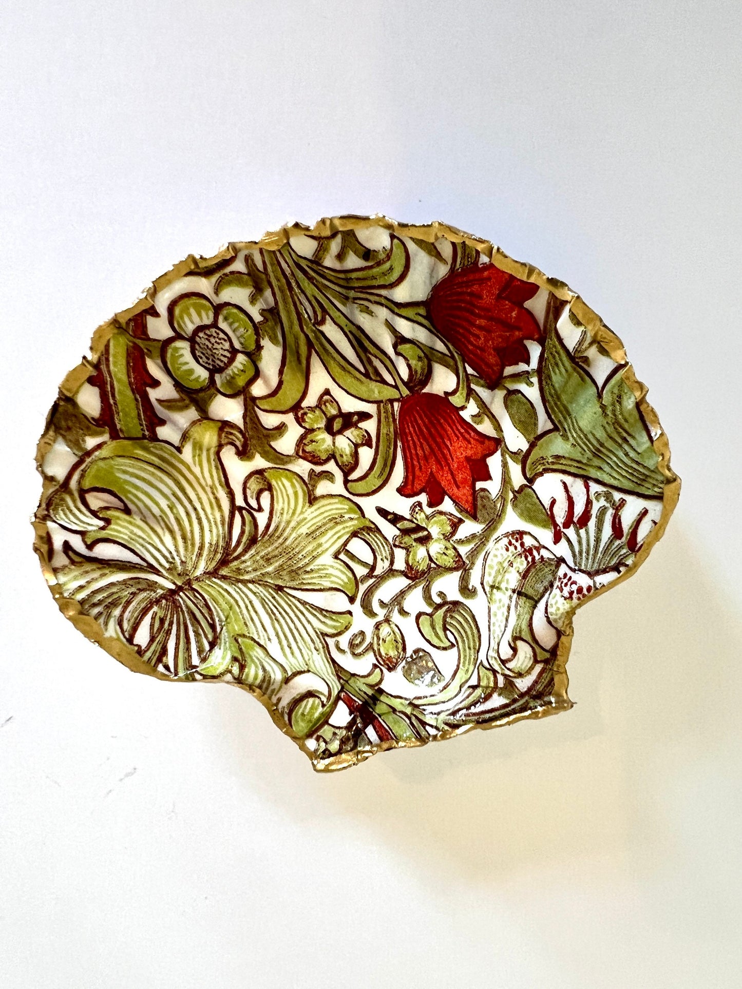Handcrafted William Morris Golden Lily scallop shell ring holder featuring an elegant botanical floral pattern in green, cream and muted red tones. Decorative Dorset shell trinket dish finished with hand-painted gold leaf edging and sealed in glossy crystal resin for a luxurious shine. Coastal inspired jewellery tray and bedside catchall perfect for rings, earrings and keepsakes. Botanical shell decor for elegant interiors, cottage style homes, thoughtful handmade gifting.