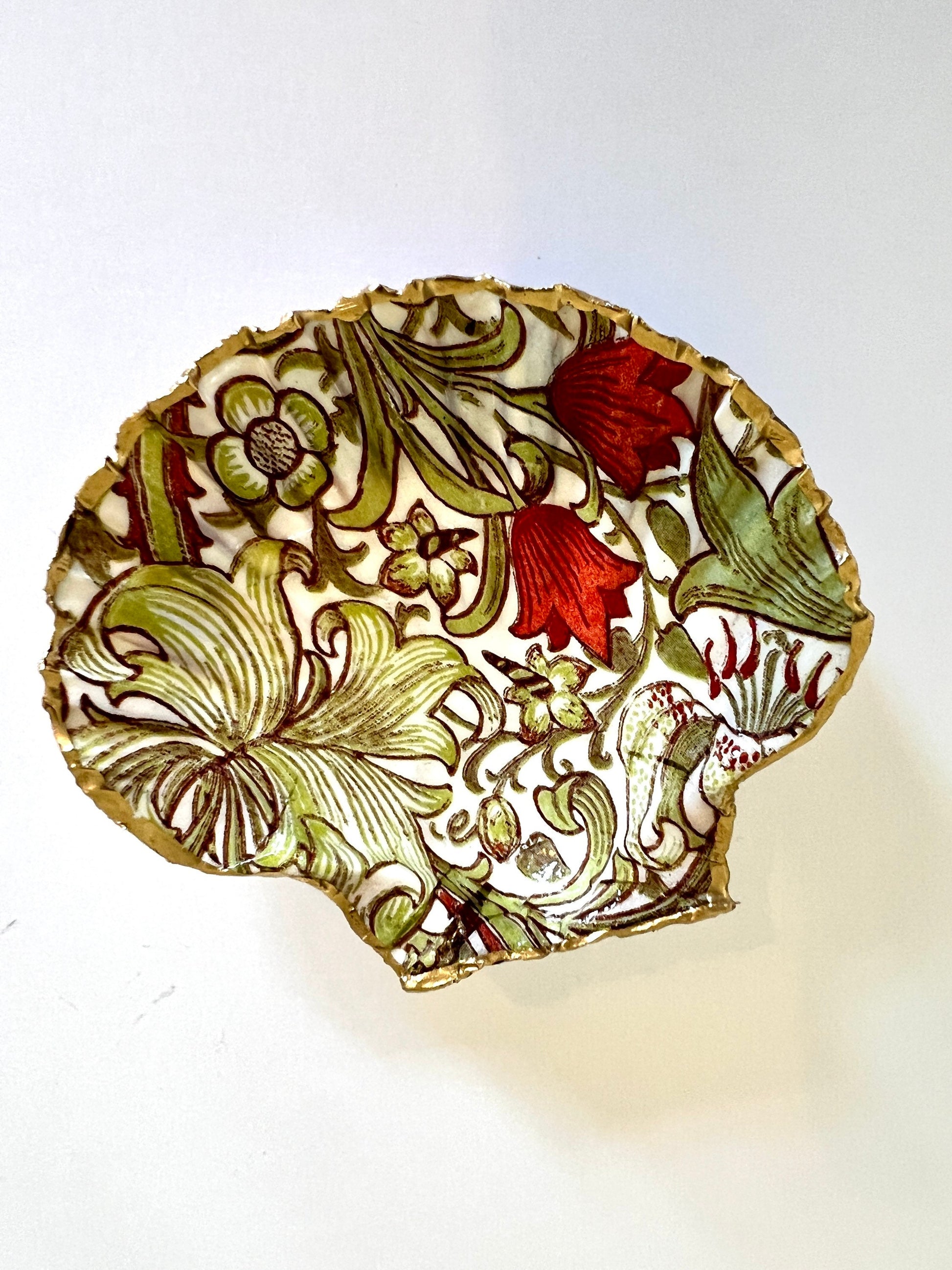Handcrafted William Morris Golden Lily scallop shell ring holder featuring an elegant botanical floral pattern in green, cream and muted red tones. Decorative Dorset shell trinket dish finished with hand-painted gold leaf edging and sealed in glossy crystal resin for a luxurious shine. Coastal inspired jewellery tray and bedside catchall perfect for rings, earrings and keepsakes. Botanical shell decor for elegant interiors, cottage style homes, thoughtful handmade gifting.