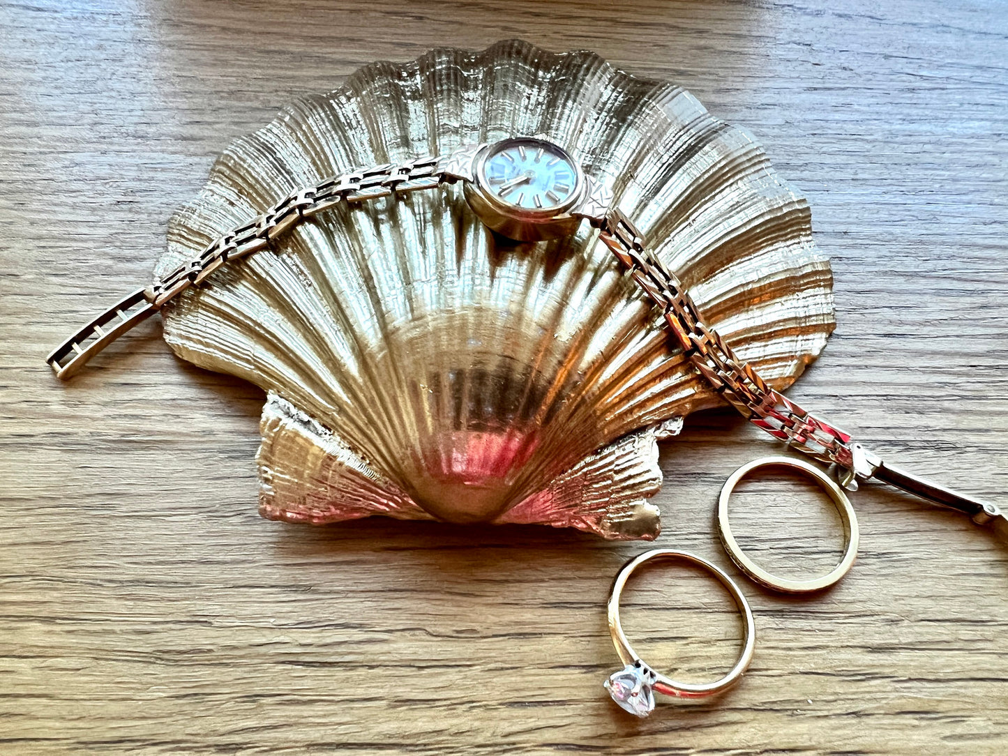 Handcrafted William Morris Golden Lily scallop shell ring holder featuring an elegant botanical floral pattern in green, cream and muted red tones. Decorative Dorset shell trinket dish finished with hand-painted gold leaf edging and sealed in glossy crystal resin for a luxurious shine. Coastal inspired jewellery tray and bedside catchall perfect for rings, earrings and keepsakes. Botanical shell decor for elegant interiors, cottage style homes, thoughtful handmade gifting.