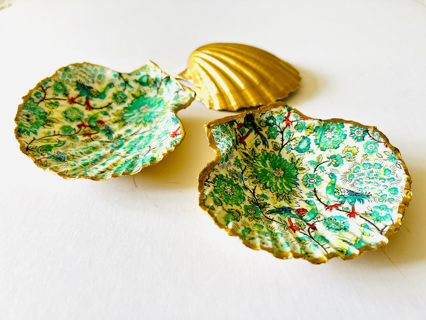 Handmade Dorset scallop shell trinket dishes featuring intricate green peacock inspired artwork in emerald, turquoise and gold tones with hand-painted gold leaf edging and glossy crystal clear resin. Elegant coastal jewellery dishes styled on a neutral background with nature inspired bird motifs and luxurious gilded detailing.