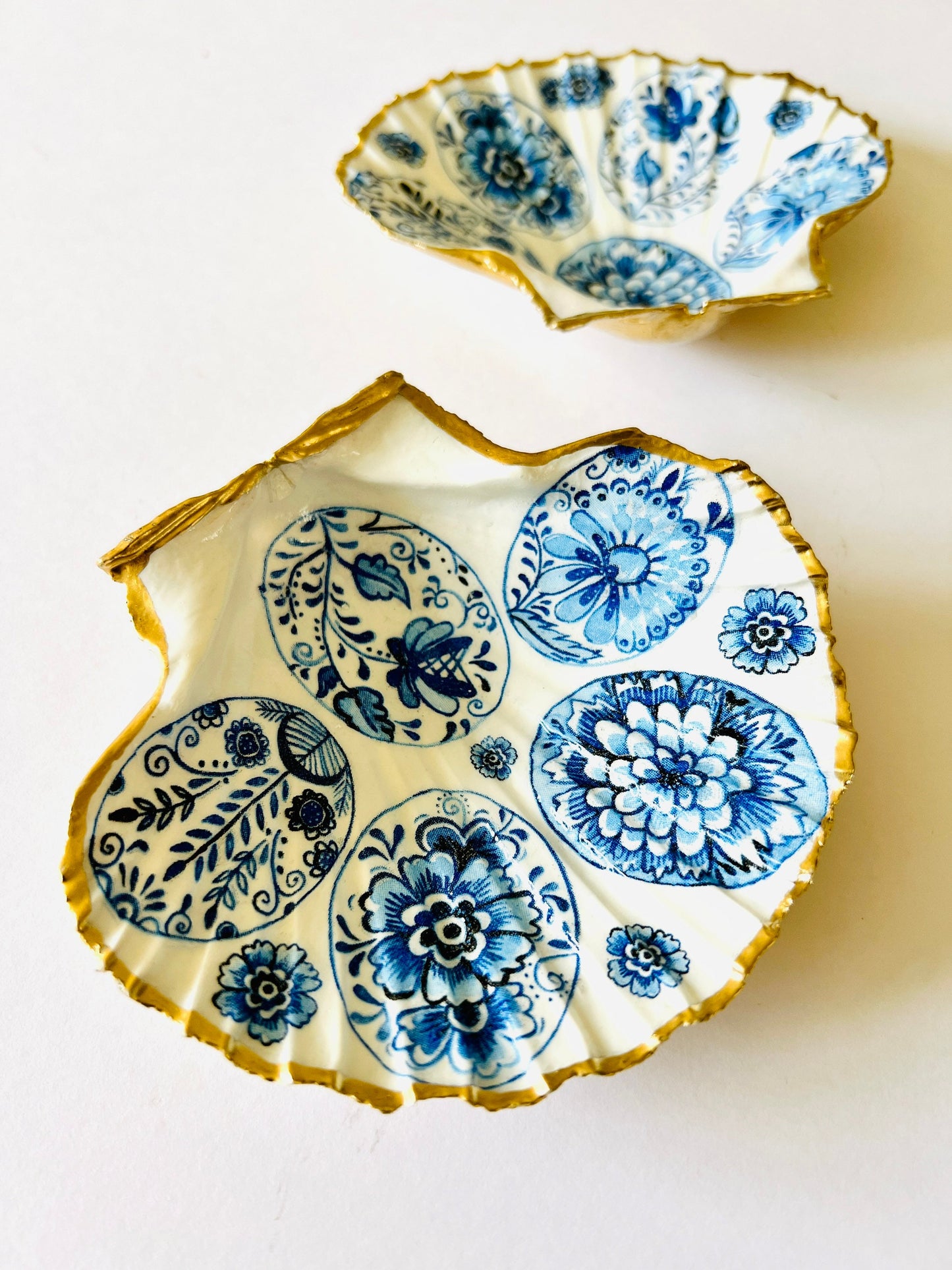 Handmade Dorset scallop shell trinket dishes featuring vintage inspired blue and white egg artwork with hand-painted gold leaf edging and glossy crystal clear resin. Elegant coastal jewellery dishes styled with Nordic and Scandinavian inspired porcelain patterns, photographed on soft neutral backgrounds with luxurious gilded detailing.