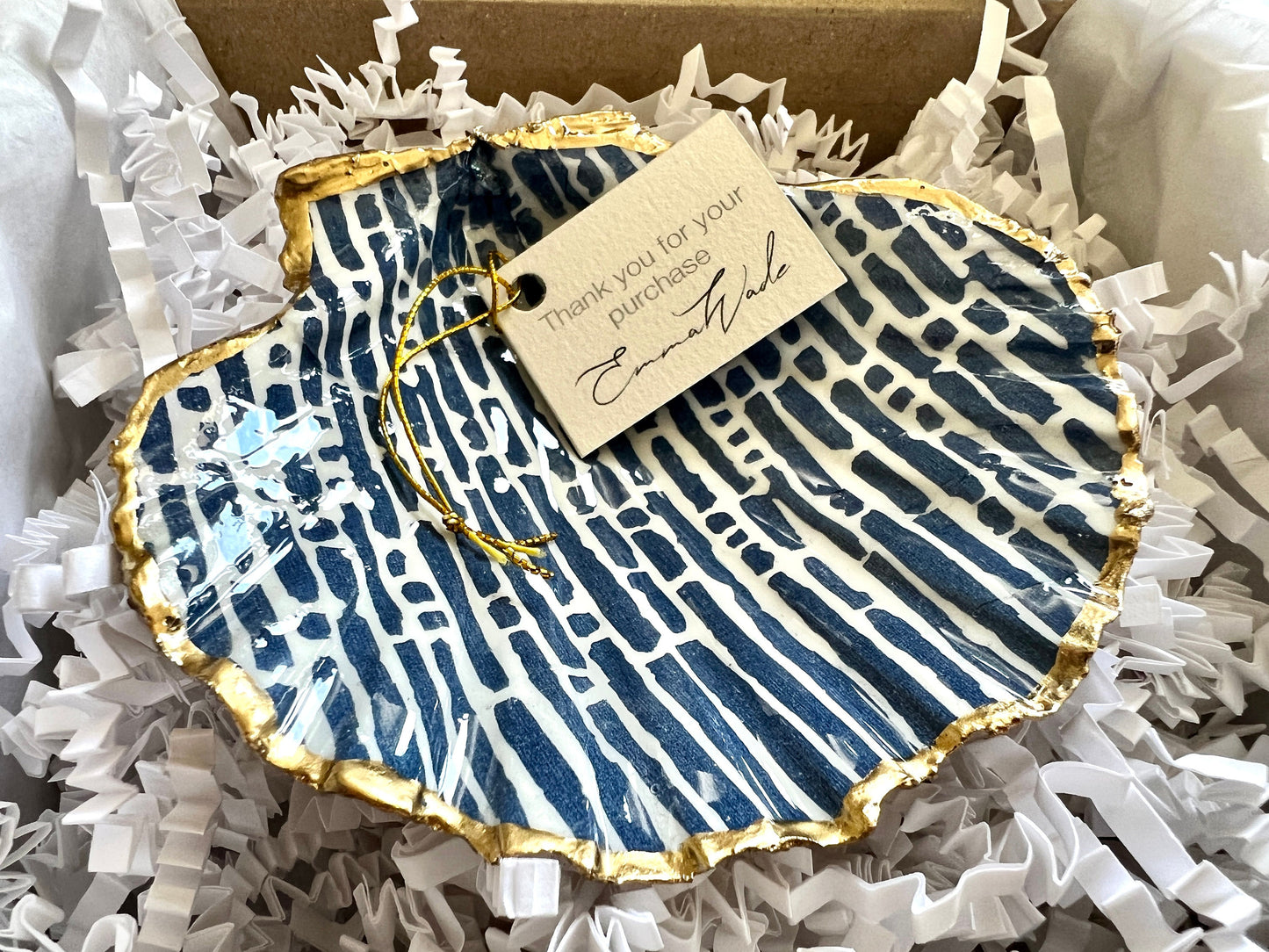 Handmade blue and white scallop shell trinket dish with gold leaf edging, crafted from a genuine Dorset shell and sealed with glossy resin. Coastal ring dish and jewellery holder featuring elegant blue line design, displayed in gift packaging. Artisan shell decor handmade in Surrey, perfect for coastal home styling, wedding gifts or nautical themed interiors.