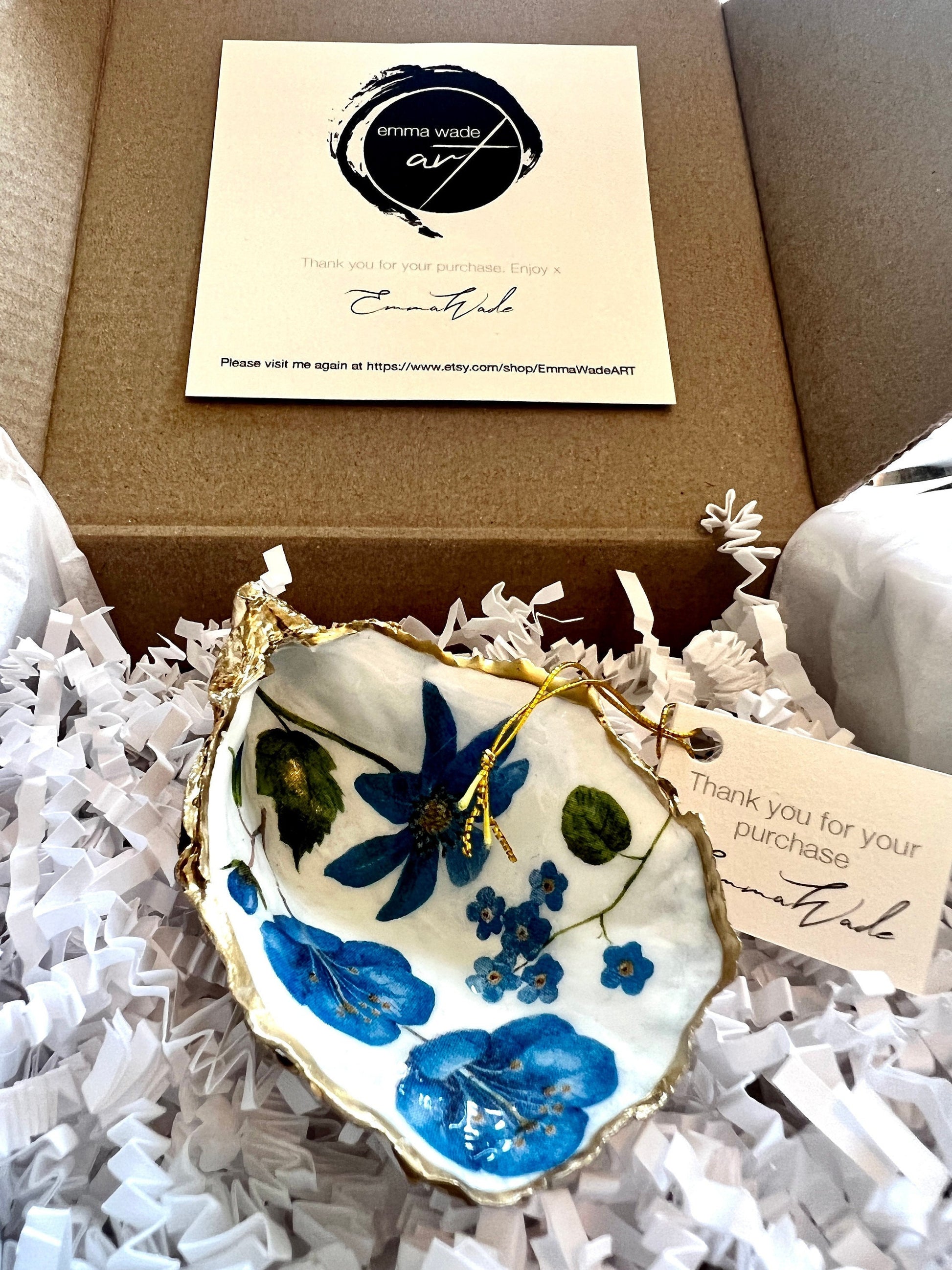 Handmade Dorset oyster shell trinket dish featuring delicate blue floral artwork including bluebells and forget-me-nots, finished with hand-applied gold leaf edging and glossy resin. Coastal-inspired jewellery dish and ring holder available in multiple sizes including XL oyster shells. Elegant handmade home décor gift ideal for birthdays, bridesmaids, Mother’s Day, weddings, and coastal interiors.