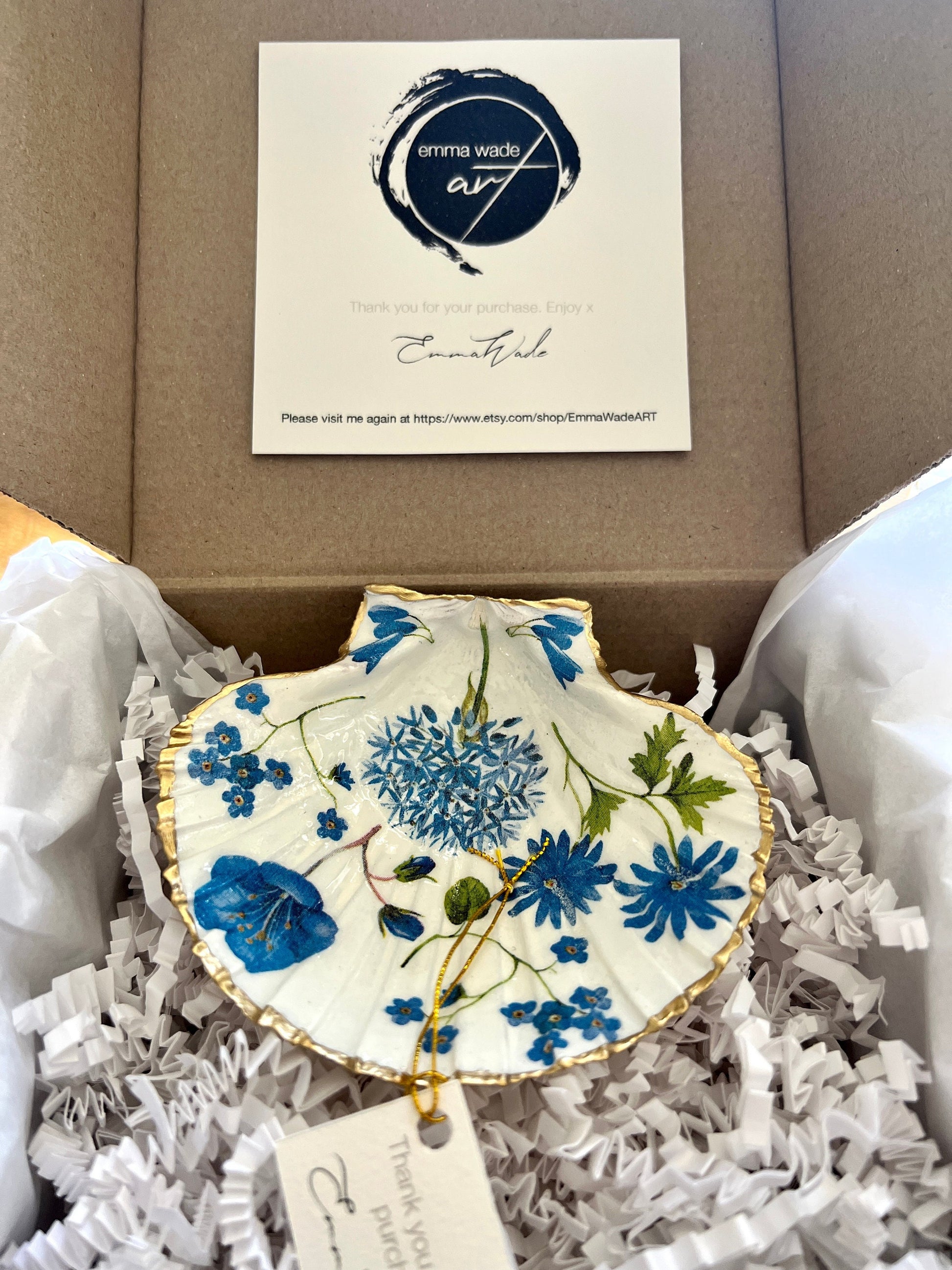 Handcrafted Dorset scallop shell trinket dish with blue spring flower design, finished with a gold leaf rim and glossy resin. The shell shows delicate blue floral motifs with green stems on a natural shell, styled on a light background. A coastal inspired jewellery or ring holder, perfect as a decorative keepsake dish, bathroom accent, or thoughtful handmade gift.