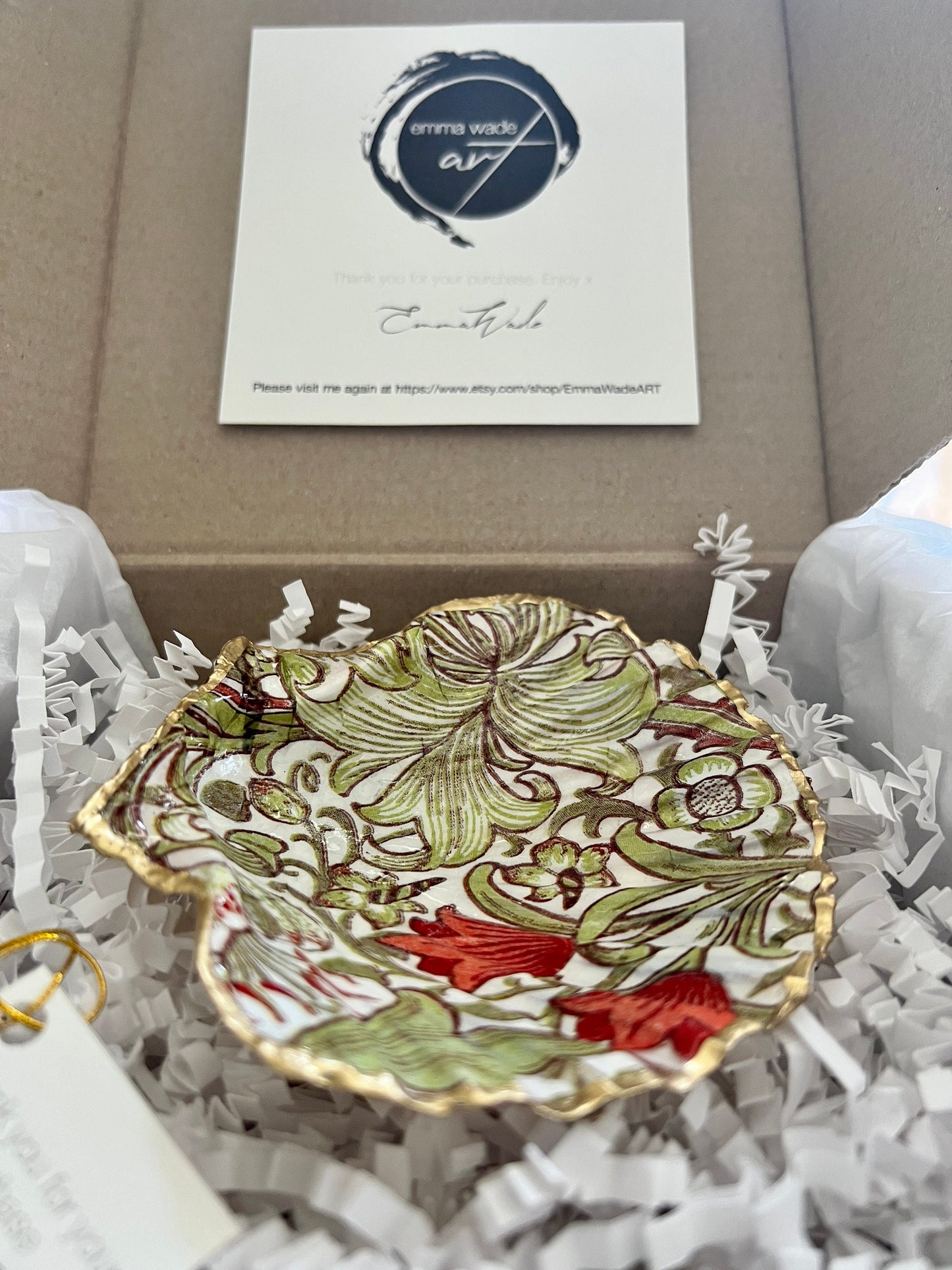 Handcrafted William Morris Golden Lily scallop shell ring holder featuring an elegant botanical floral pattern in green, cream and muted red tones. Decorative Dorset shell trinket dish finished with hand-painted gold leaf edging and sealed in glossy crystal resin for a luxurious shine. Coastal inspired jewellery tray and bedside catchall perfect for rings, earrings and keepsakes. Botanical shell decor for elegant interiors, cottage style homes, thoughtful handmade gifting.