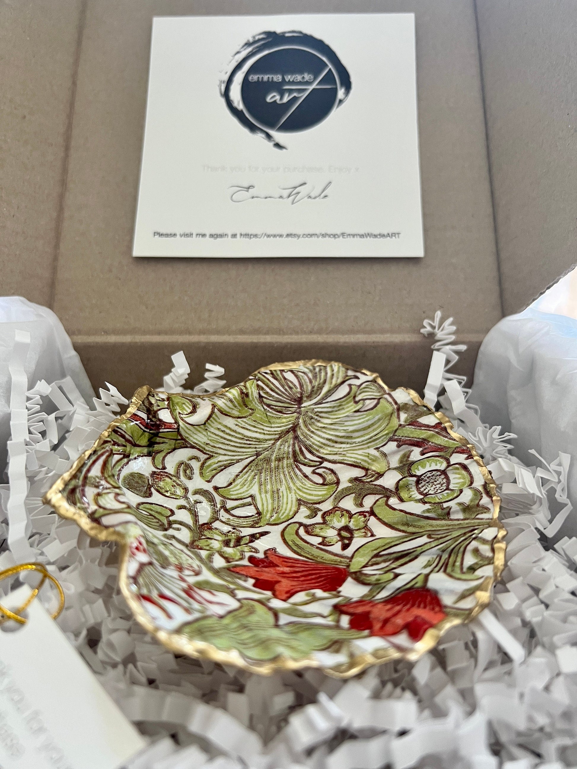 Handcrafted William Morris Golden Lily scallop shell ring holder featuring an elegant botanical floral pattern in green, cream and muted red tones. Decorative Dorset shell trinket dish finished with hand-painted gold leaf edging and sealed in glossy crystal resin for a luxurious shine. Coastal inspired jewellery tray and bedside catchall perfect for rings, earrings and keepsakes. Botanical shell decor for elegant interiors, cottage style homes, thoughtful handmade gifting.