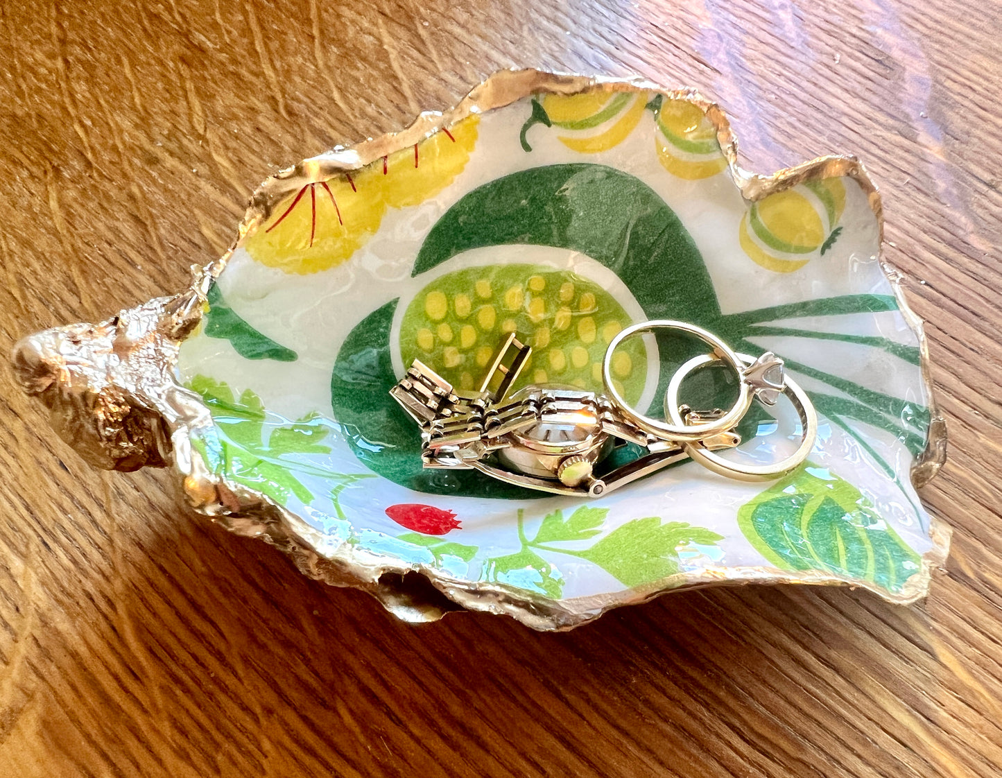Handmade Dorset oyster shell trinket dish featuring colourful garden fruit artwork in green, yellow, and red tones with hand-gilded gold leaf edging and glossy resin finish. Coastal jewellery holder and botanical home décor gift.