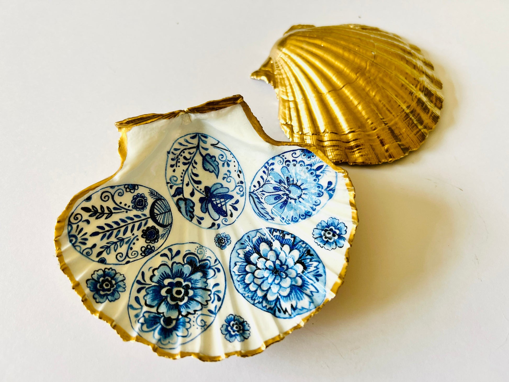 Handmade Dorset scallop shell trinket dishes featuring vintage inspired blue and white egg artwork with hand-painted gold leaf edging and glossy crystal clear resin. Elegant coastal jewellery dishes styled with Nordic and Scandinavian inspired porcelain patterns, photographed on soft neutral backgrounds with luxurious gilded detailing.