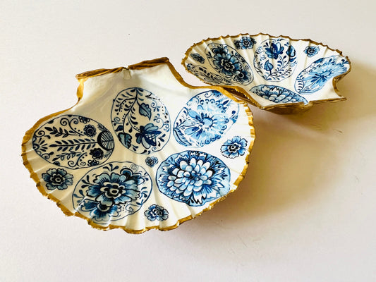 Handmade Dorset scallop shell trinket dishes featuring vintage inspired blue and white egg artwork with hand-painted gold leaf edging and glossy crystal clear resin. Elegant coastal jewellery dishes styled with Nordic and Scandinavian inspired porcelain patterns, photographed on soft neutral backgrounds with luxurious gilded detailing.