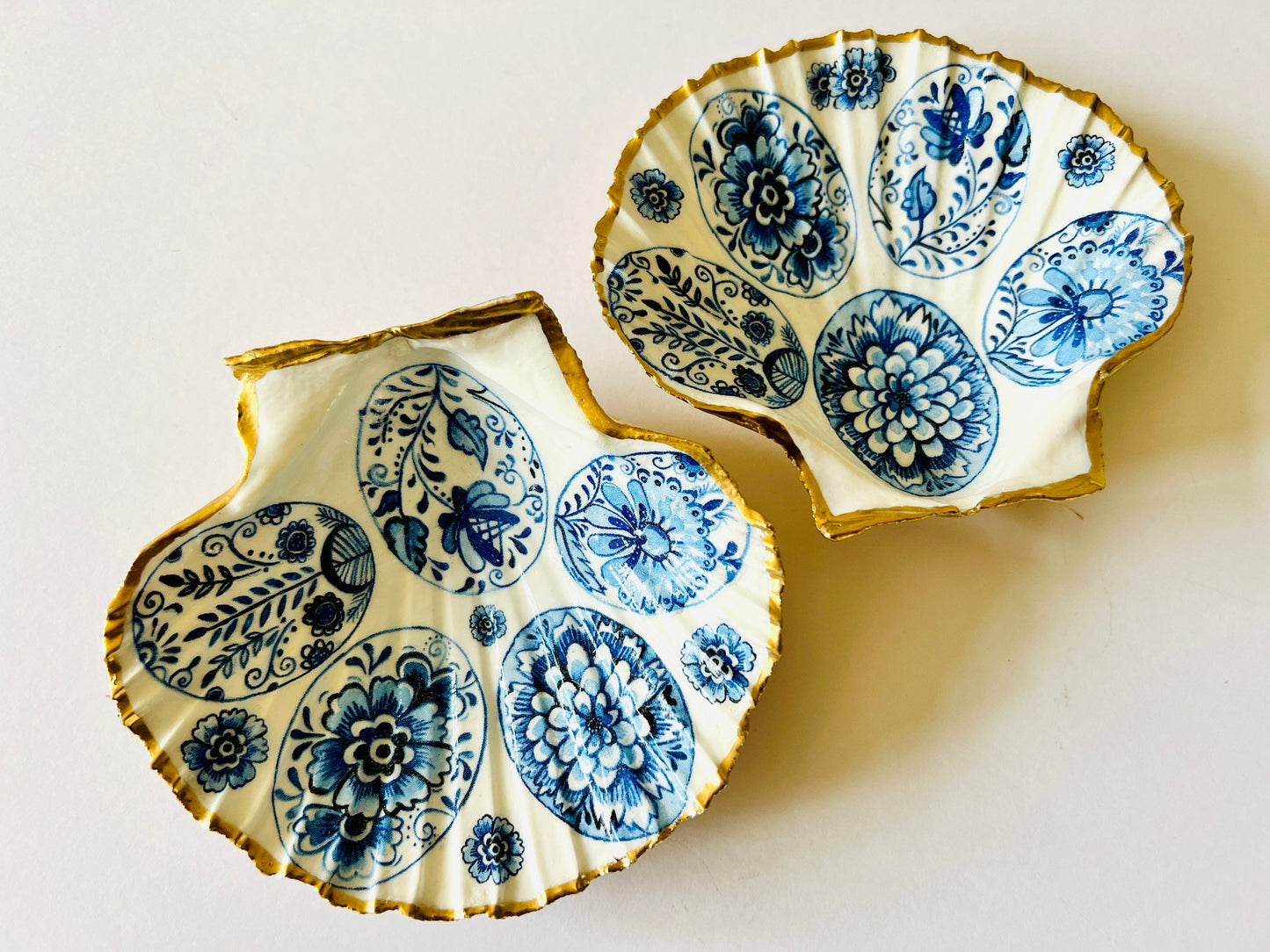 Handmade Dorset scallop shell trinket dishes featuring vintage inspired blue and white egg artwork with hand-painted gold leaf edging and glossy crystal clear resin. Elegant coastal jewellery dishes styled with Nordic and Scandinavian inspired porcelain patterns, photographed on soft neutral backgrounds with luxurious gilded detailing.