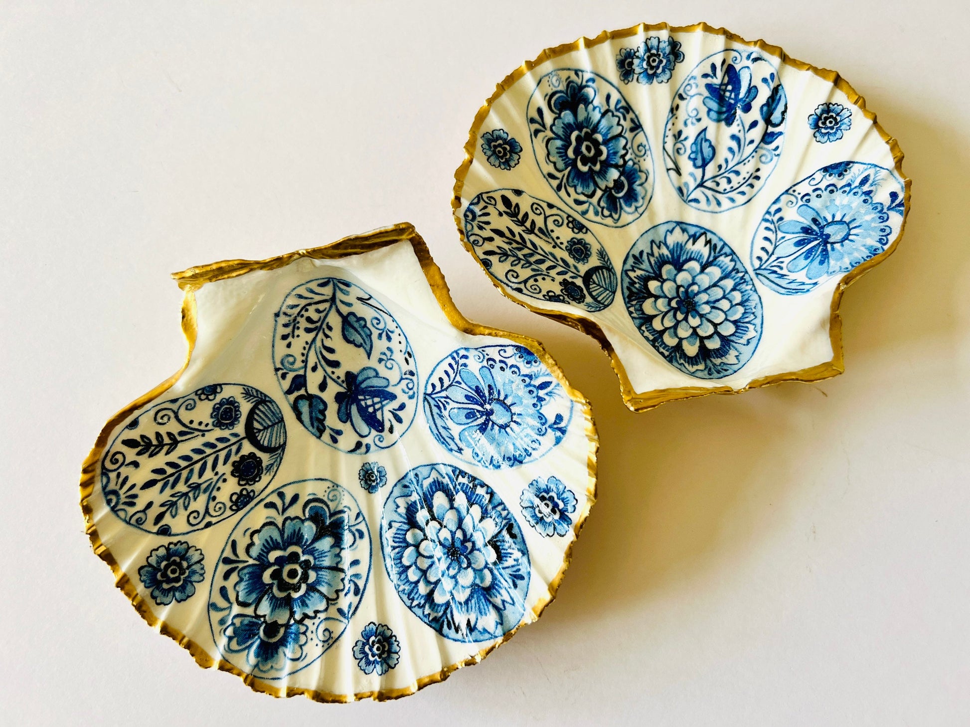 Handmade Dorset scallop shell trinket dishes featuring vintage inspired blue and white egg artwork with hand-painted gold leaf edging and glossy crystal clear resin. Elegant coastal jewellery dishes styled with Nordic and Scandinavian inspired porcelain patterns, photographed on soft neutral backgrounds with luxurious gilded detailing.