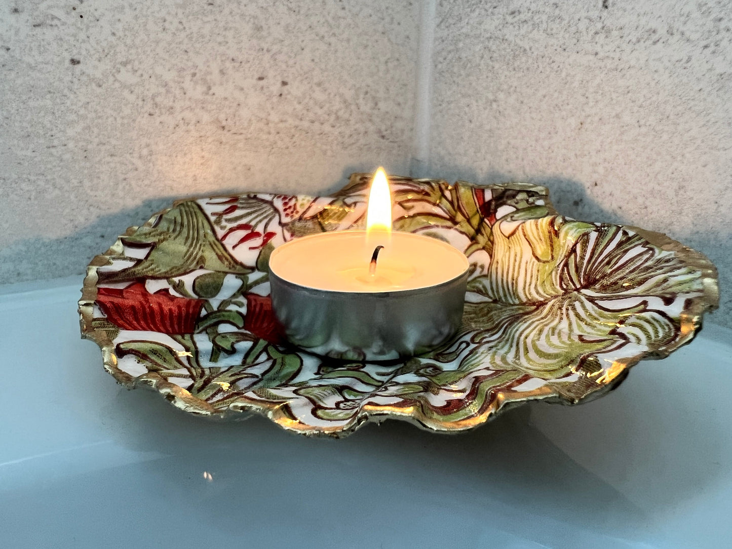 Handcrafted William Morris Golden Lily scallop shell ring holder featuring an elegant botanical floral pattern in green, cream and muted red tones. Decorative Dorset shell trinket dish finished with hand-painted gold leaf edging and sealed in glossy crystal resin for a luxurious shine. Coastal inspired jewellery tray and bedside catchall perfect for rings, earrings and keepsakes. Botanical shell decor for elegant interiors, cottage style homes, thoughtful handmade gifting.