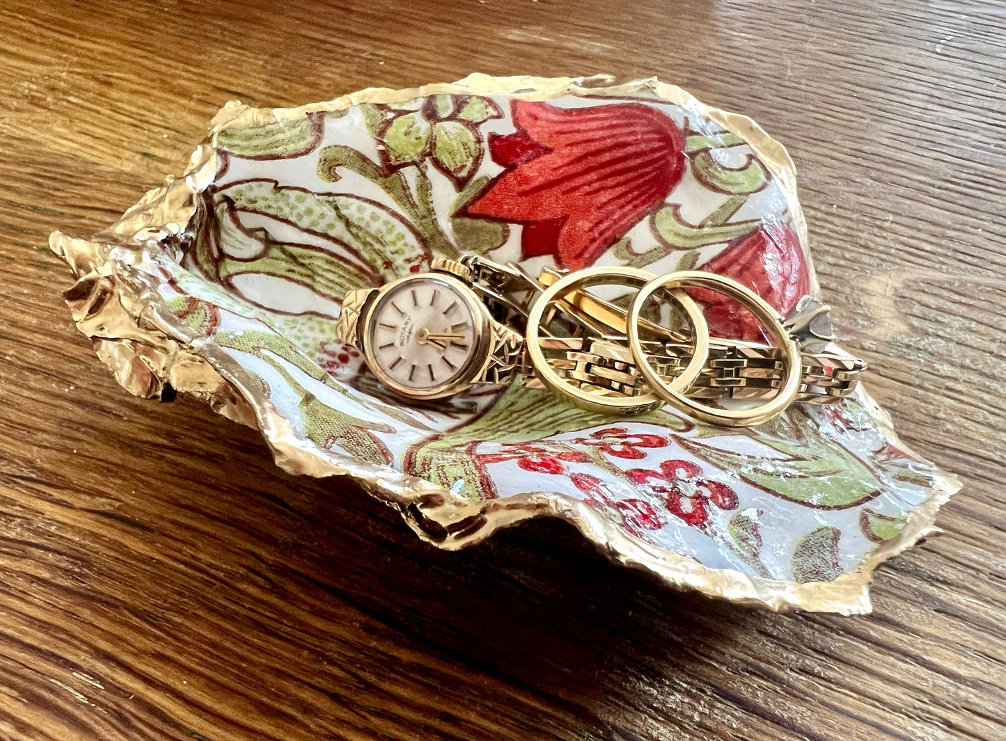 Handmade Dorset oyster shell ring dish featuring William Morris Golden Lily floral artwork in green, red and gold tones. Natural oyster shell trinket dish with pearlescent interior, hand-finished liquid gold leaf edging and glossy resin coating. Decorative jewellery holder and coastal heritage gift inspired by classic William Morris interiors and Arts and Crafts design.