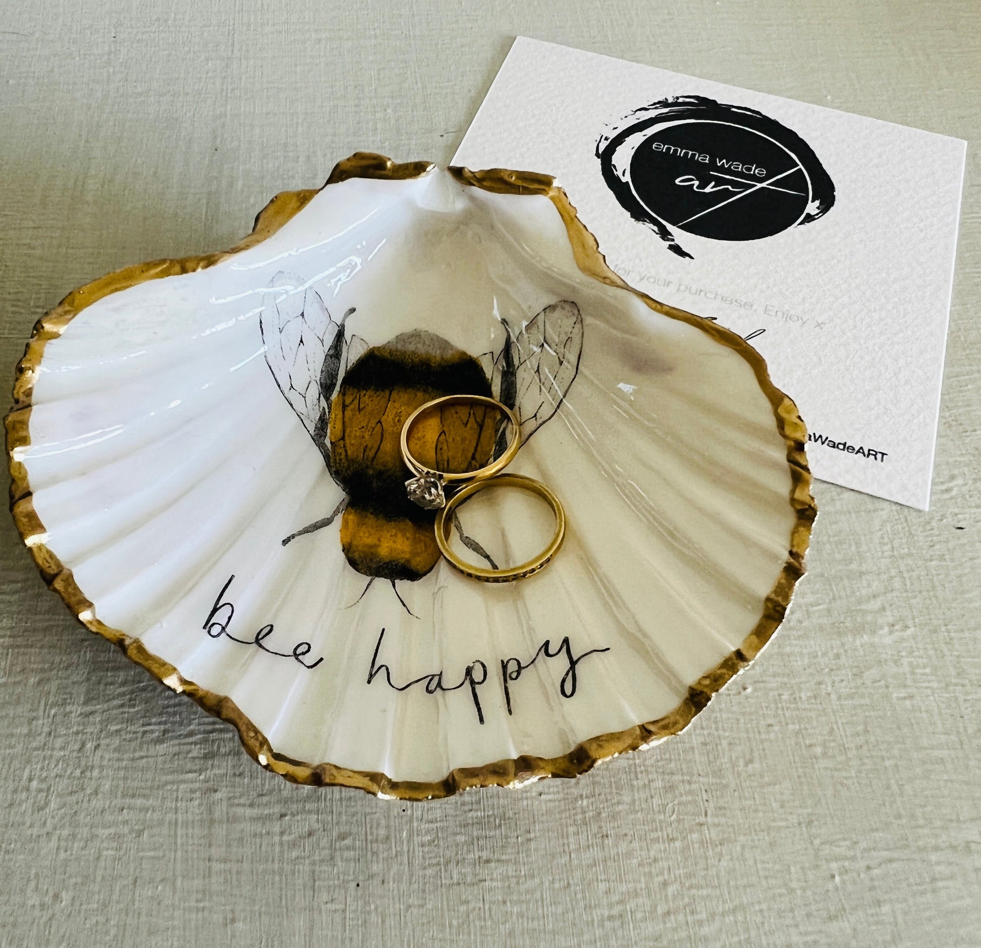 Handmade scallop shell trinket dish featuring a bumblebee illustration with gold leaf edging and glossy resin finish. Coastal jewellery dish in natural white shell with bee artwork, displayed as a ring holder and handmade bee lover gift
