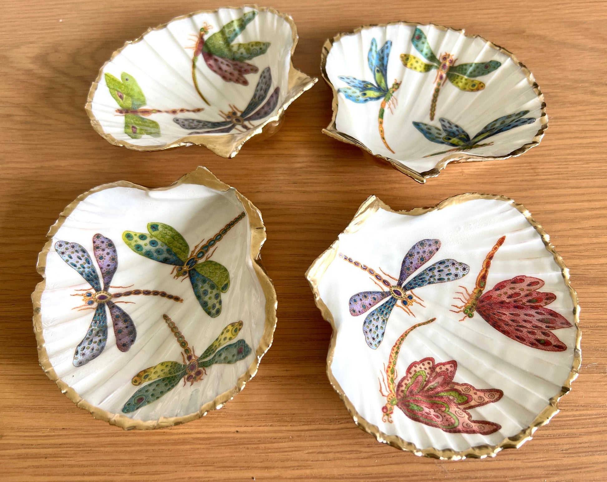 Handmade dragonfly scallop shell trinket dish with gold leaf edging and glossy resin finish. Coastal jewellery and ring dish crafted from a natural Dorset scallop shell, featuring colourful dragonfly artwork. Decorative shell bowl photographed on a light background, showing the natural shell shape and shimmering gilded edges, ideal for holding rings, earrings, trinkets or small treasures.
