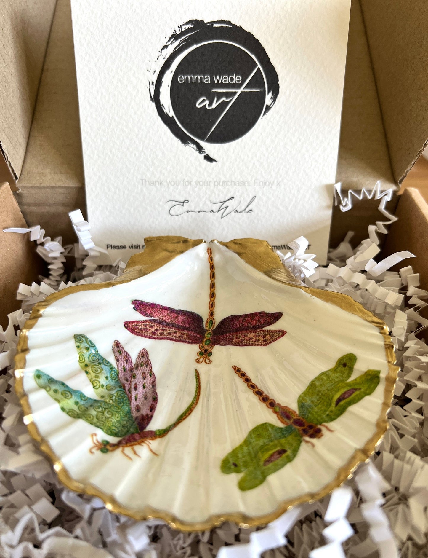 Handmade dragonfly scallop shell trinket dish with gold leaf edging and glossy resin finish. Coastal jewellery and ring dish crafted from a natural Dorset scallop shell, featuring colourful dragonfly artwork. Decorative shell bowl photographed on a light background, showing the natural shell shape and shimmering gilded edges, ideal for holding rings, earrings, trinkets or small treasures.