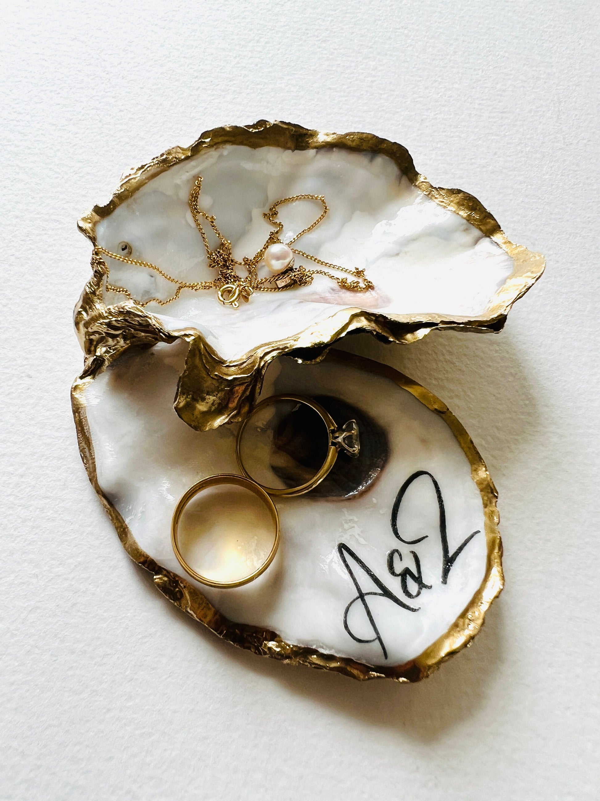 Handmade Dorset oyster shell jewellery dish set with a cupped oyster shell resting on a flat shell base, finished with natural pearl interiors and gold leaf edging. Personalised coastal trinket dish handcrafted in the UK, ideal for holding rings or jewellery. Elegant shell decor presented in sustainable gift packaging, perfect for weddings, anniversaries or special occasions.