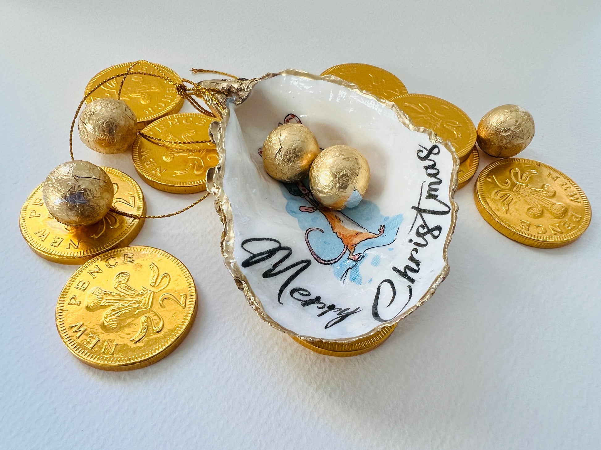 Handmade Dorset oyster shell Christmas ornament featuring a whimsical festive mouse illustration with gold leaf edging, glossy resin finish, and hanging ribbon. Coastal Christmas decoration styled as a luxury handmade oyster shell bauble and festive trinket keepsake gift.