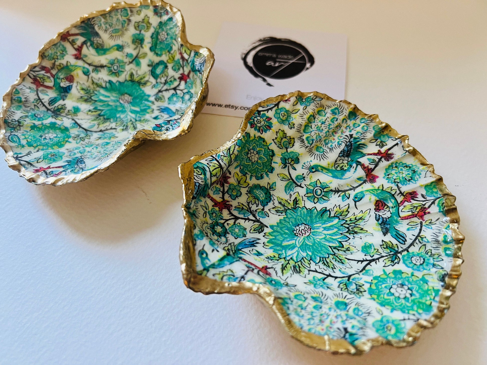 Handmade Dorset scallop shell trinket dishes featuring intricate green peacock inspired artwork in emerald, turquoise and gold tones with hand-painted gold leaf edging and glossy crystal clear resin. Elegant coastal jewellery dishes styled on a neutral background with nature inspired bird motifs and luxurious gilded detailing.
