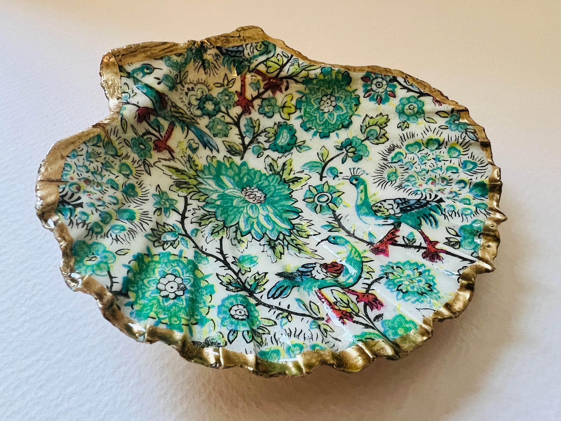 Handmade Dorset scallop shell trinket dishes featuring intricate green peacock inspired artwork in emerald, turquoise and gold tones with hand-painted gold leaf edging and glossy crystal clear resin. Elegant coastal jewellery dishes styled on a neutral background with nature inspired bird motifs and luxurious gilded detailing.
